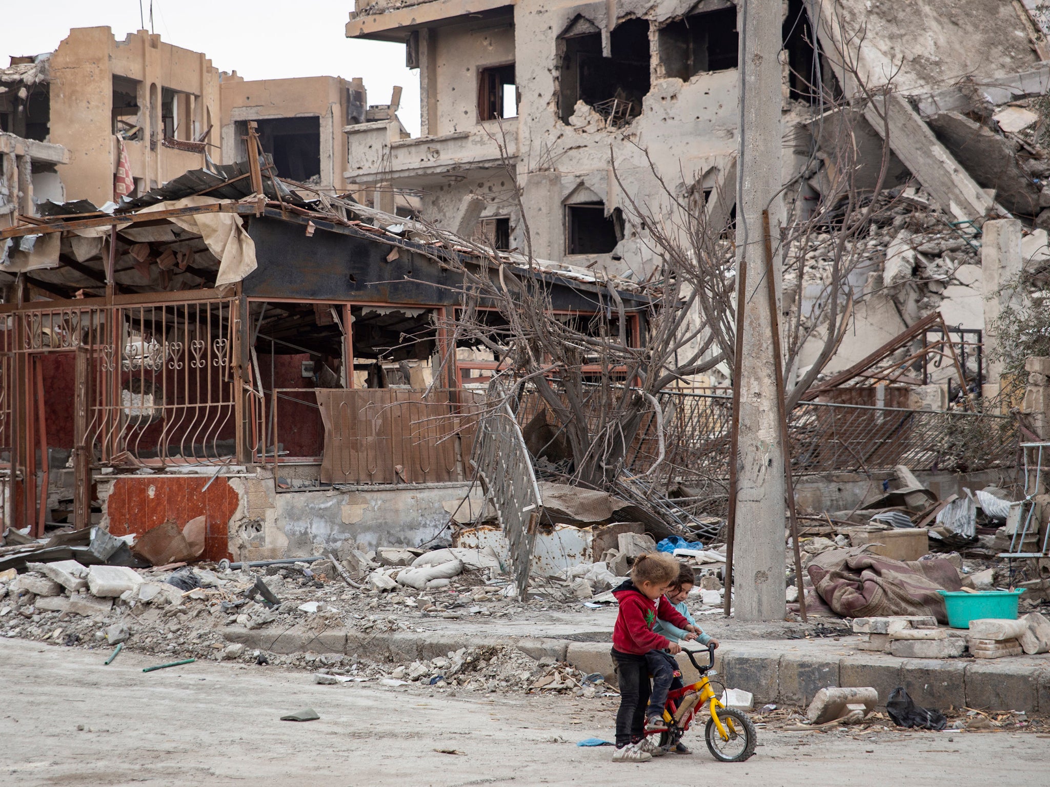 Children riding a bicycle next to destroyed buildings in Raqqa