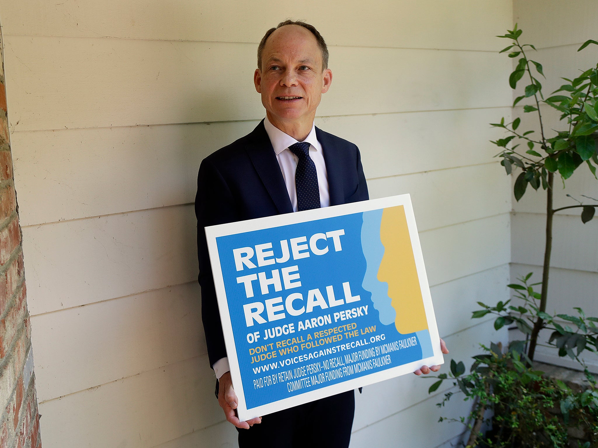 Judge Aaron Persky poses for a photo with a sign opposing his recall in Los Altos Hills, California