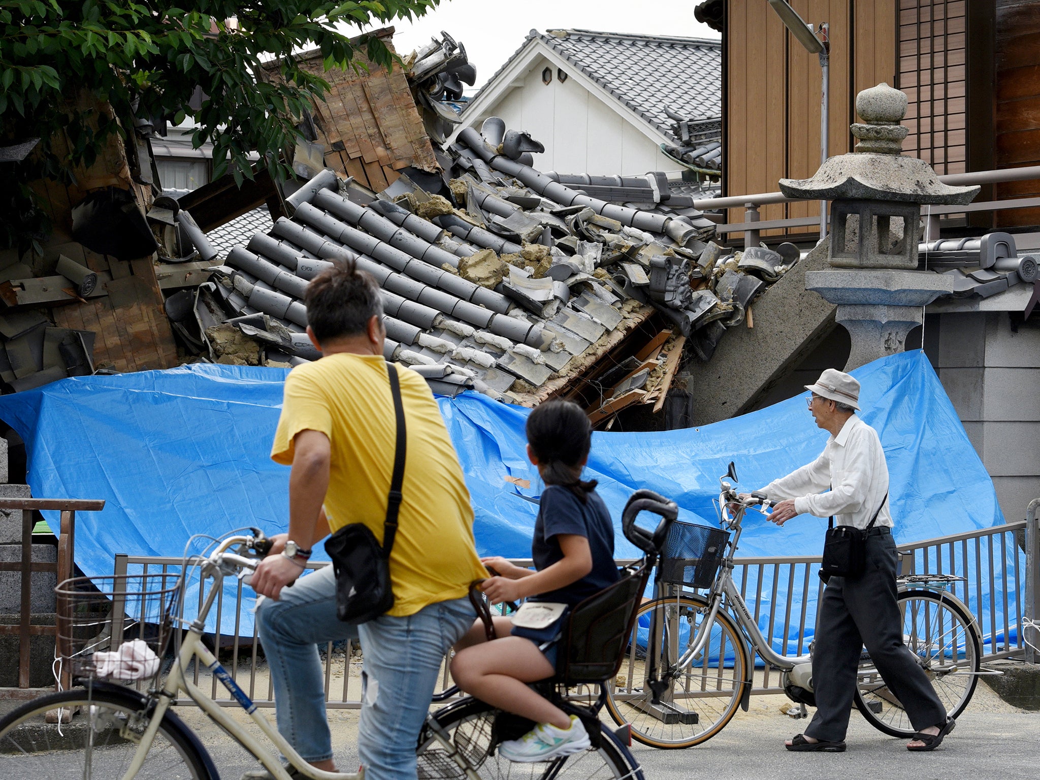 Residents pass by a temple gate collapsed by an earthquake in Ibaraki, Osaka Prefecture, western Japan. The earthquake, which struck western Japan, killed three people injured more than 50.