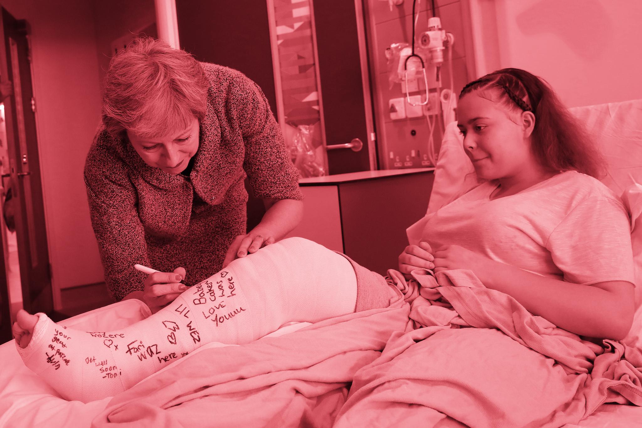 Britain's Prime Minister Theresa May signs the pot of patient Jade Myers, 15 of London, who broke her leg falling off a wall, during a visit to The Royal Free Hospital on June 18, 2018 in London, England