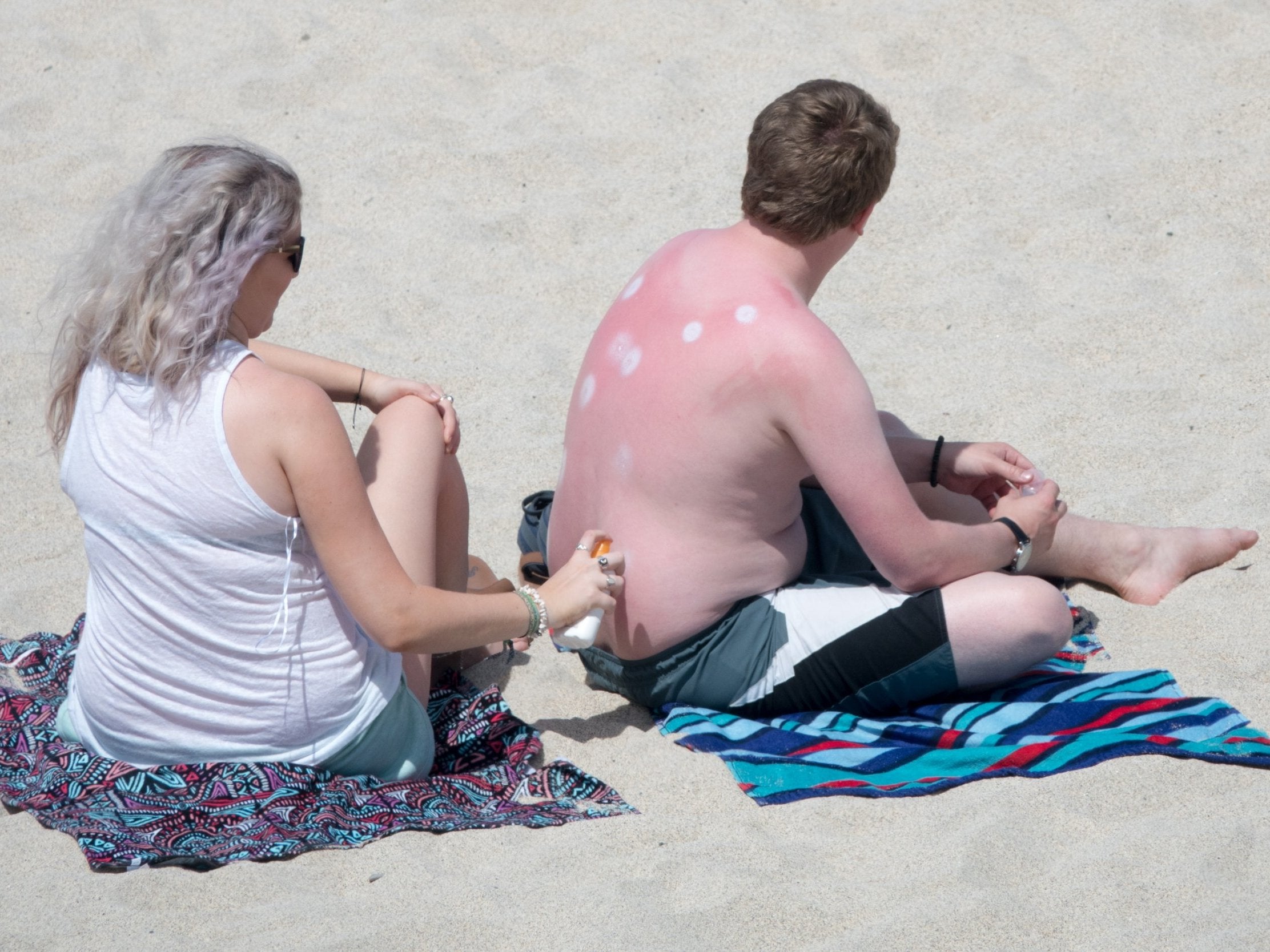 A woman applies sun lotion to a man's back as they enjoy the fine weather on Porthmeor Beach, St Ives, on Thursday