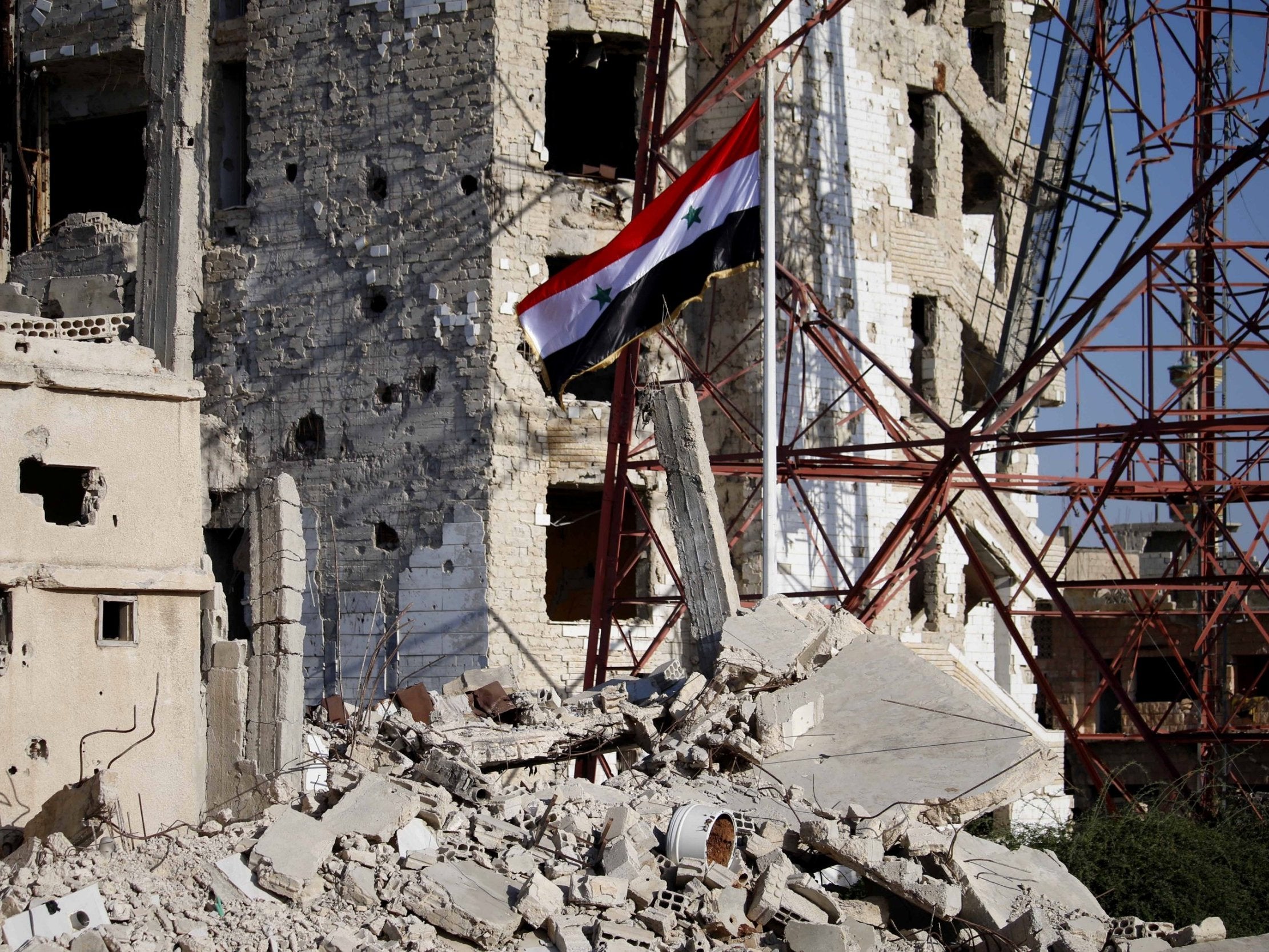 The Syrian national flag rises in the midst of damaged buildings in Deraa