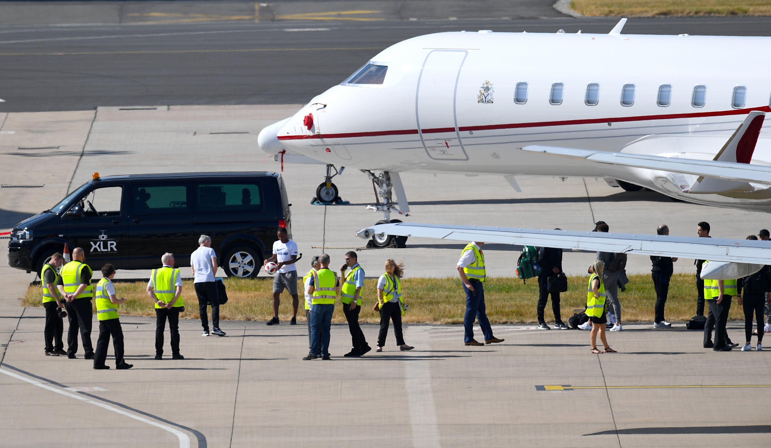 Raheem Sterling (centre) leaves the plane after it touched down, surrounded by security officers