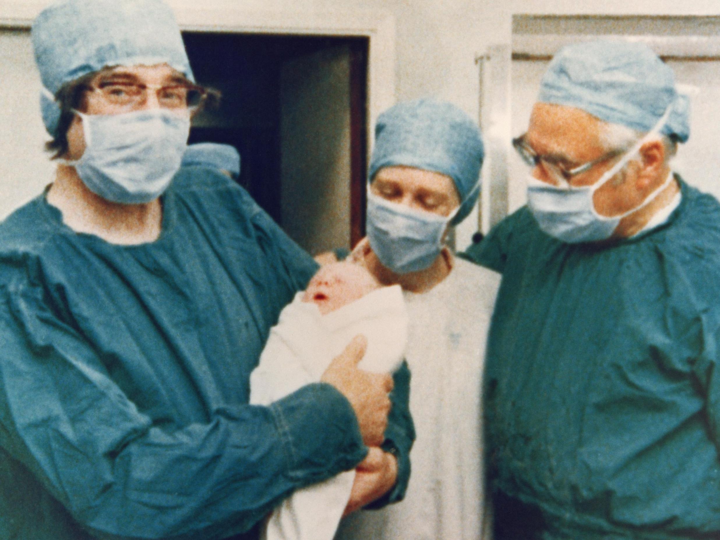 Dr Robert Edwards holding the newborn baby with mother Lesley Brown and obstetrician Dr Patrick Steptoe looking on