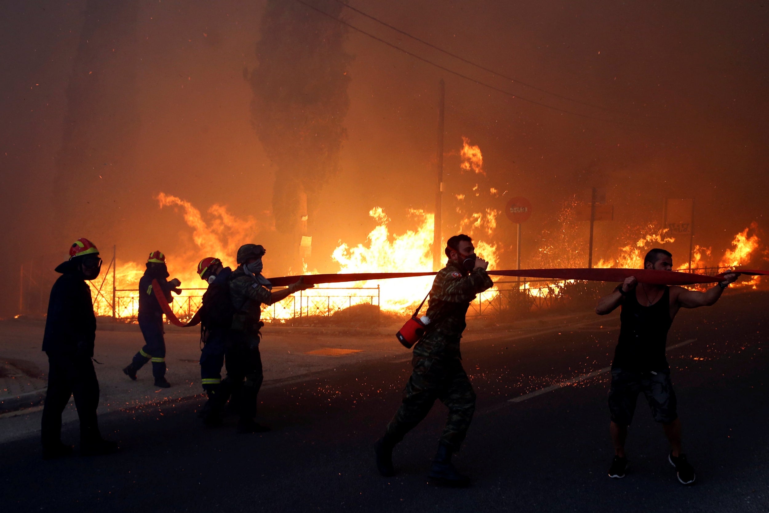 Firefighters, soldiers and local residents carry a hose as a wildfire burns in the town of Rafina, near Athens, Greece