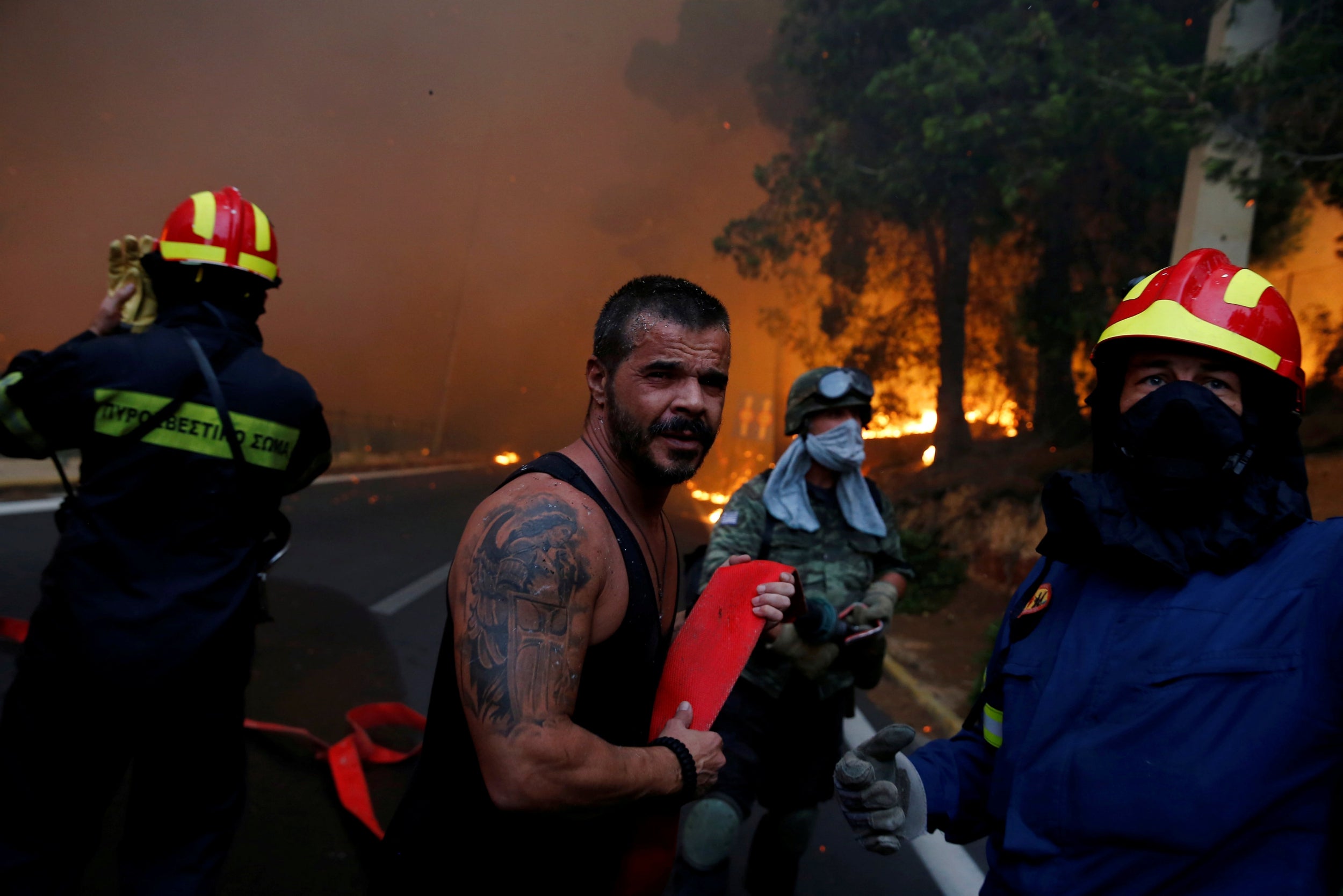 Firefighters, soldiers and local residents carry a hose as a wildfire burns in the town of Rafina, near Athens, Greece, in 2018