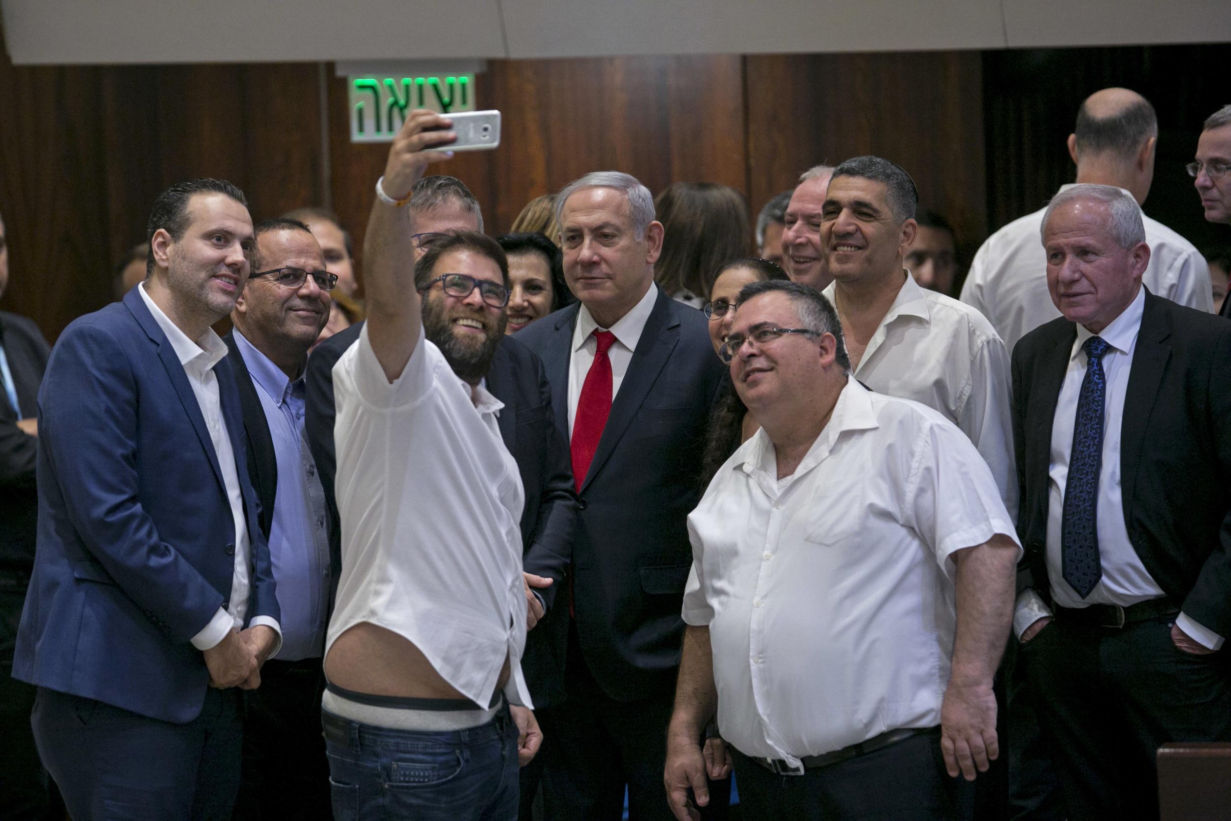 Knesset member Oren Hazan takes a selfie with Israel’s prime Minister Benjamin Netanyahu, centre, and MP David Bitan, right of Netanyahu, after a Knesset session passed the contentious nation state bill on 19 July 2018