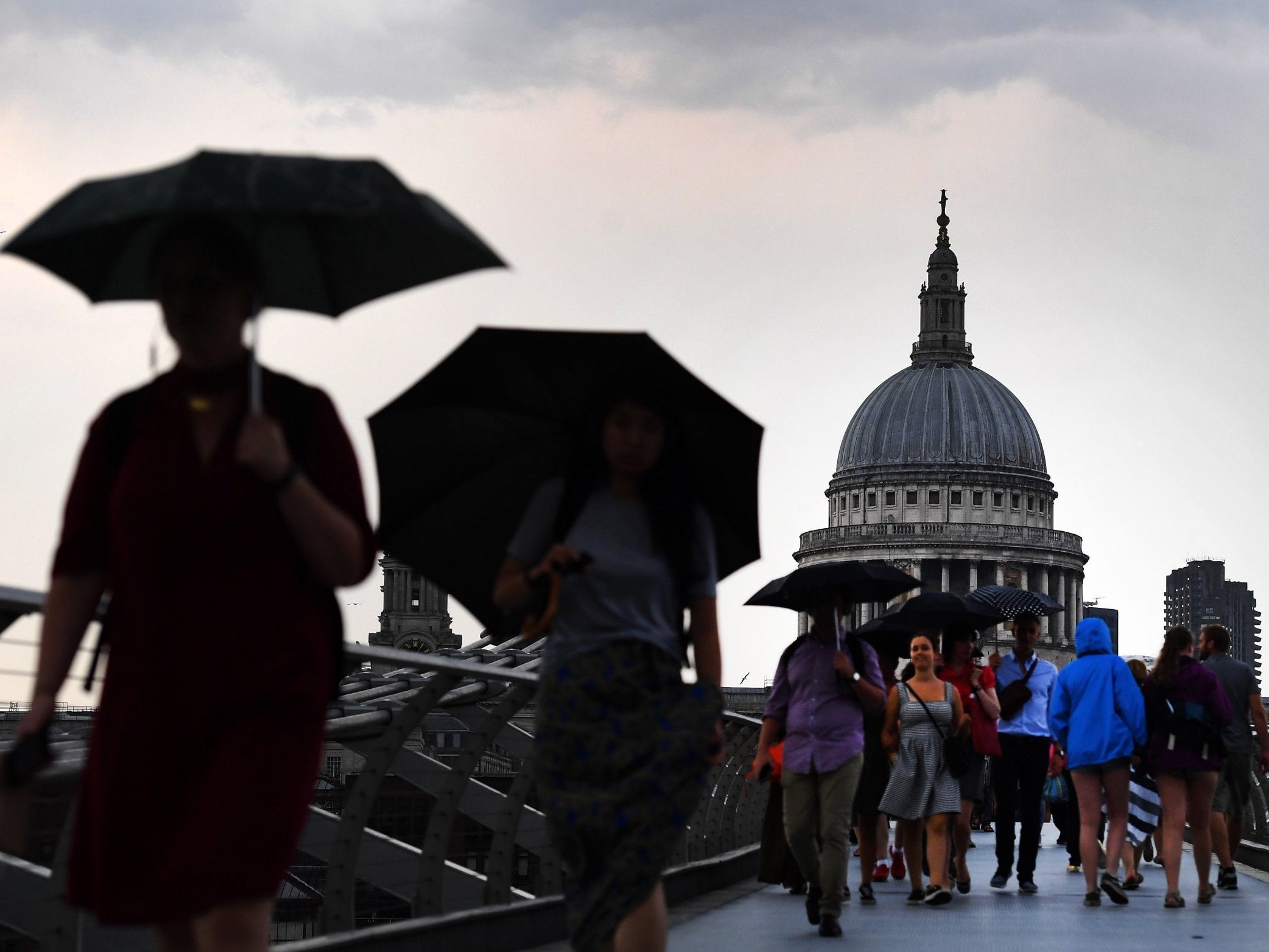 Umbrellas come out on the Millennium Bridge in London as rain brings an end to the hot weather