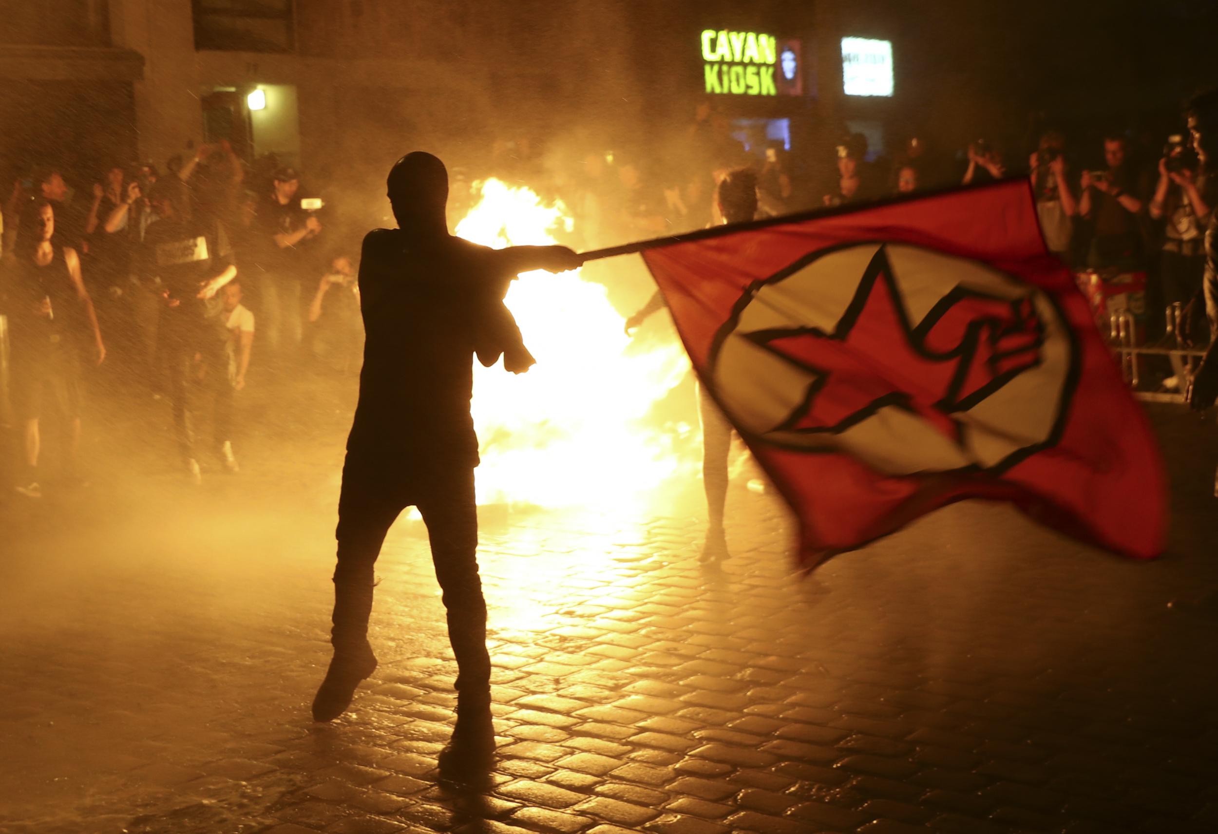 An anti-G20 protester waves a flag in front of burning garbage following clashes with German riot police in Hamburg, Germany, July 6, 2017.