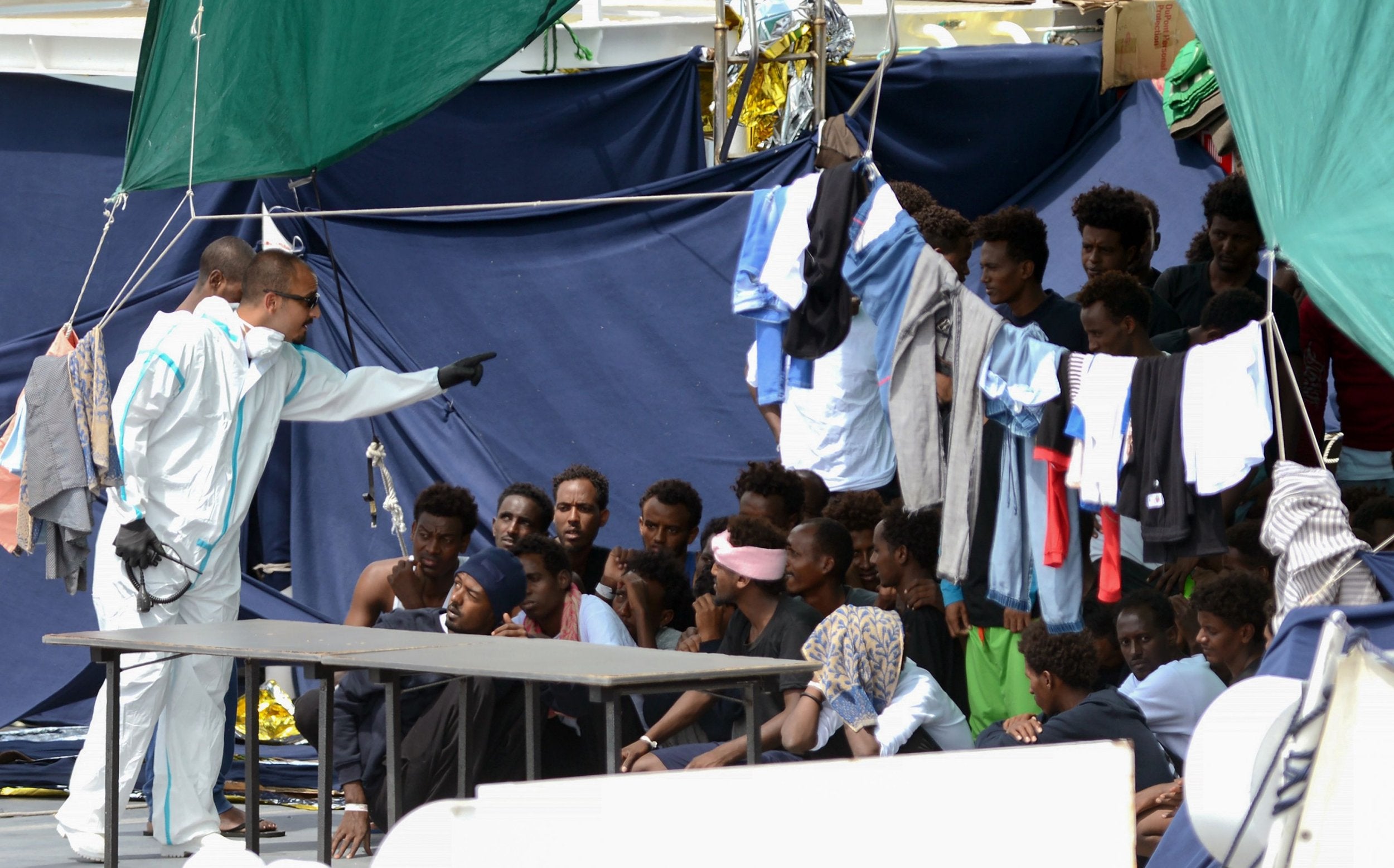 An official in a protective suit gesturing to detainees of the ‘Diciotti‘ vessel on Thursday