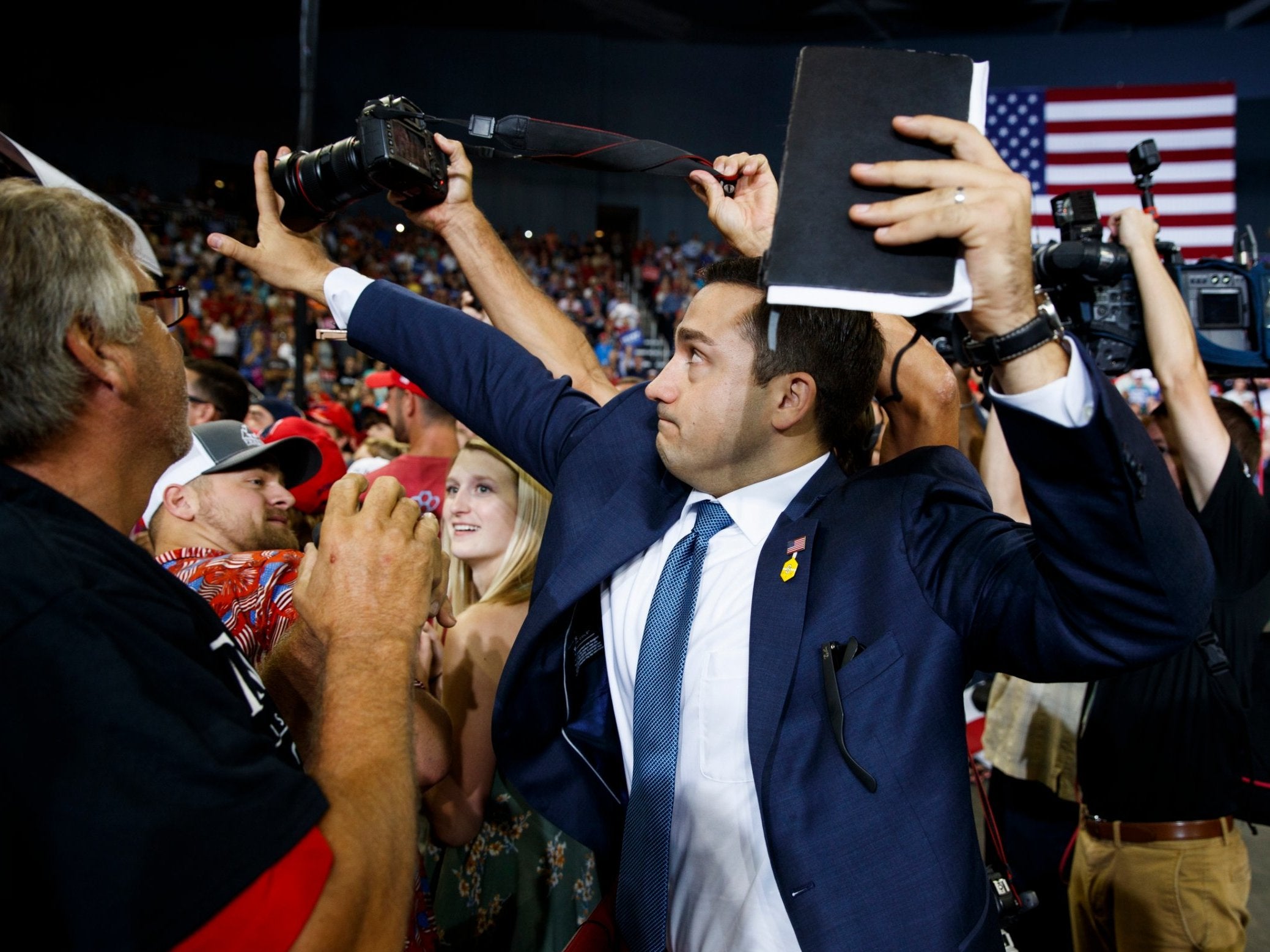 A volunteer member of the advance team for president Donald Trump blocks a camera as a photojournalist attempts to take a photo of a protester during a campaign rally