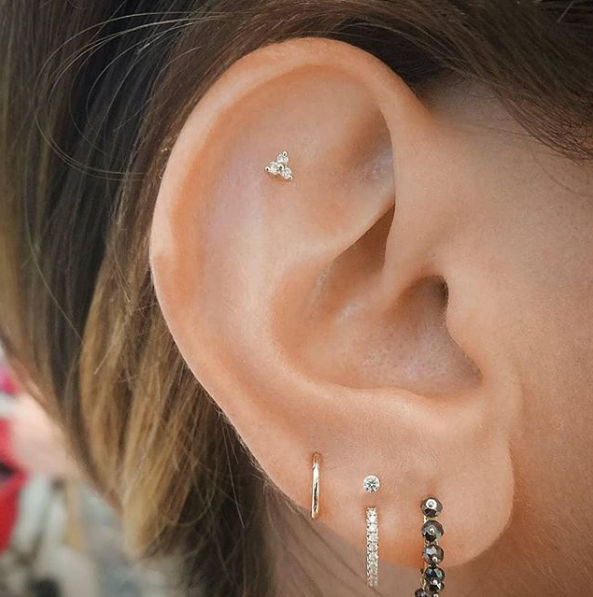 A high lobe piercing with a diamond stud, seen above the middle ring