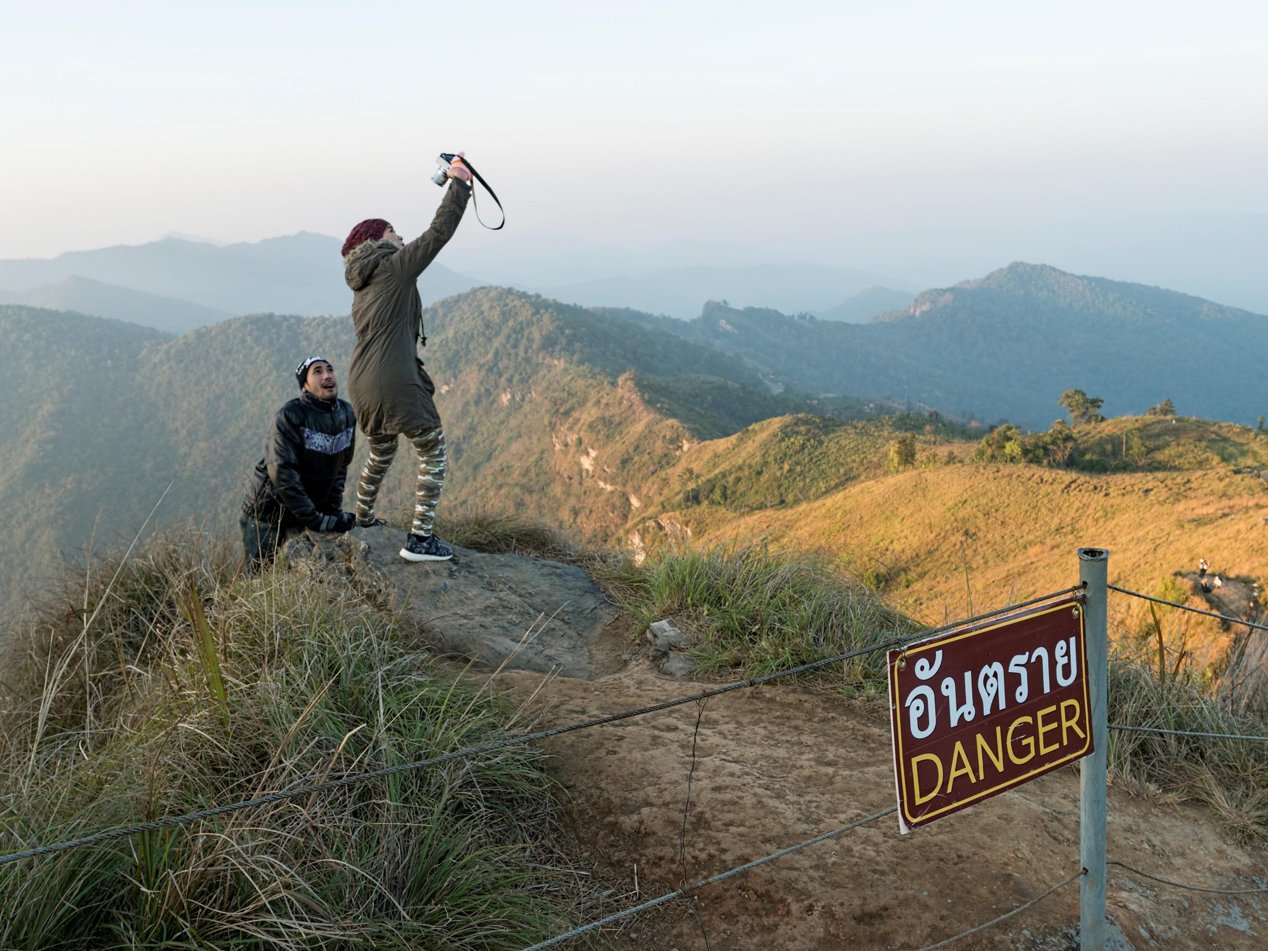 A couple ignore the danger sign to take selfies on a precarious ledge in Thailand’s mountainous Phu Chee Fah area