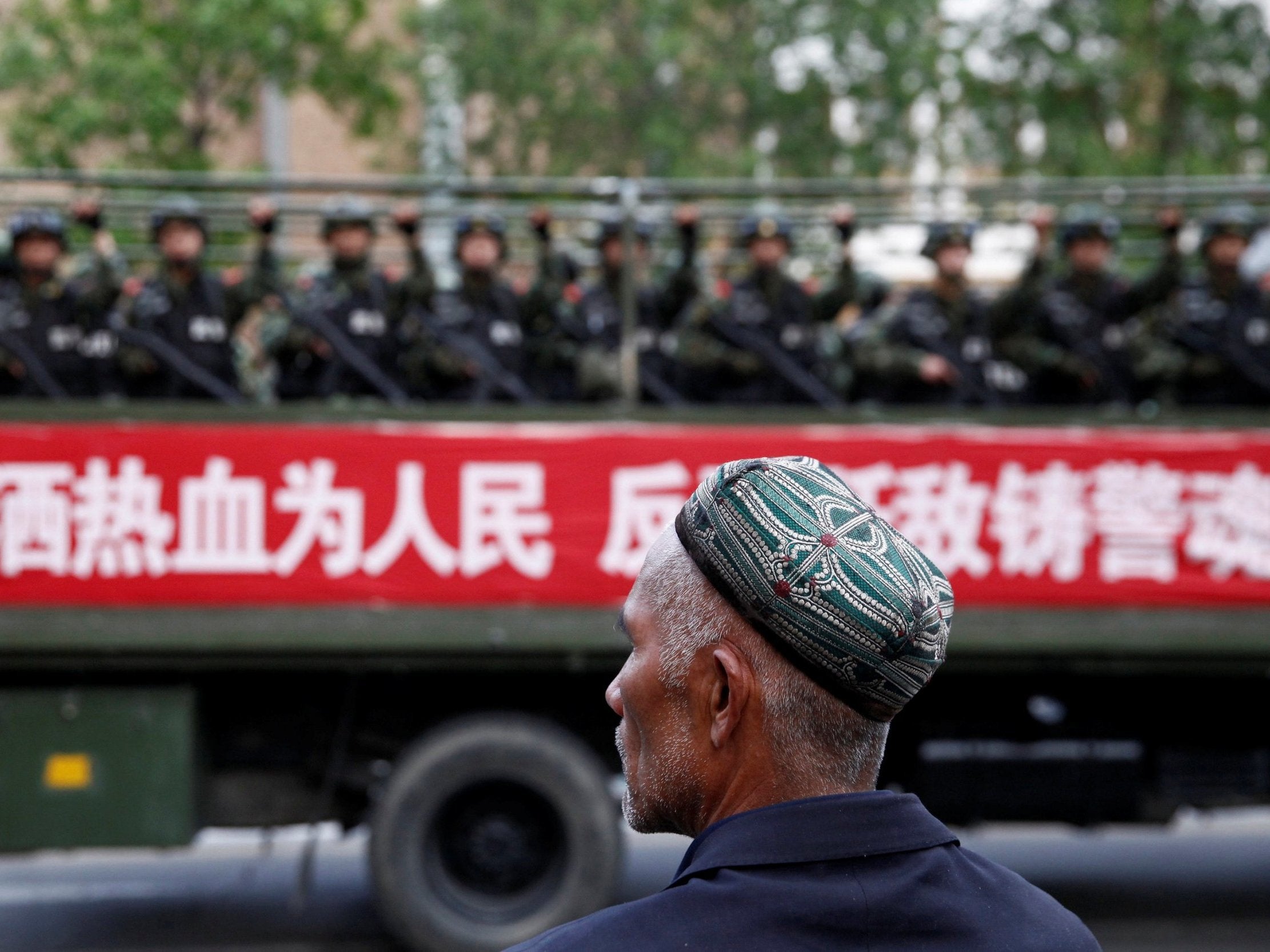 An Uighur man looks on as a truck carrying paramilitary policemen travels along a street during an anti-terrorism oath-taking rally in Urumqi, Xinjiang (Reuters)