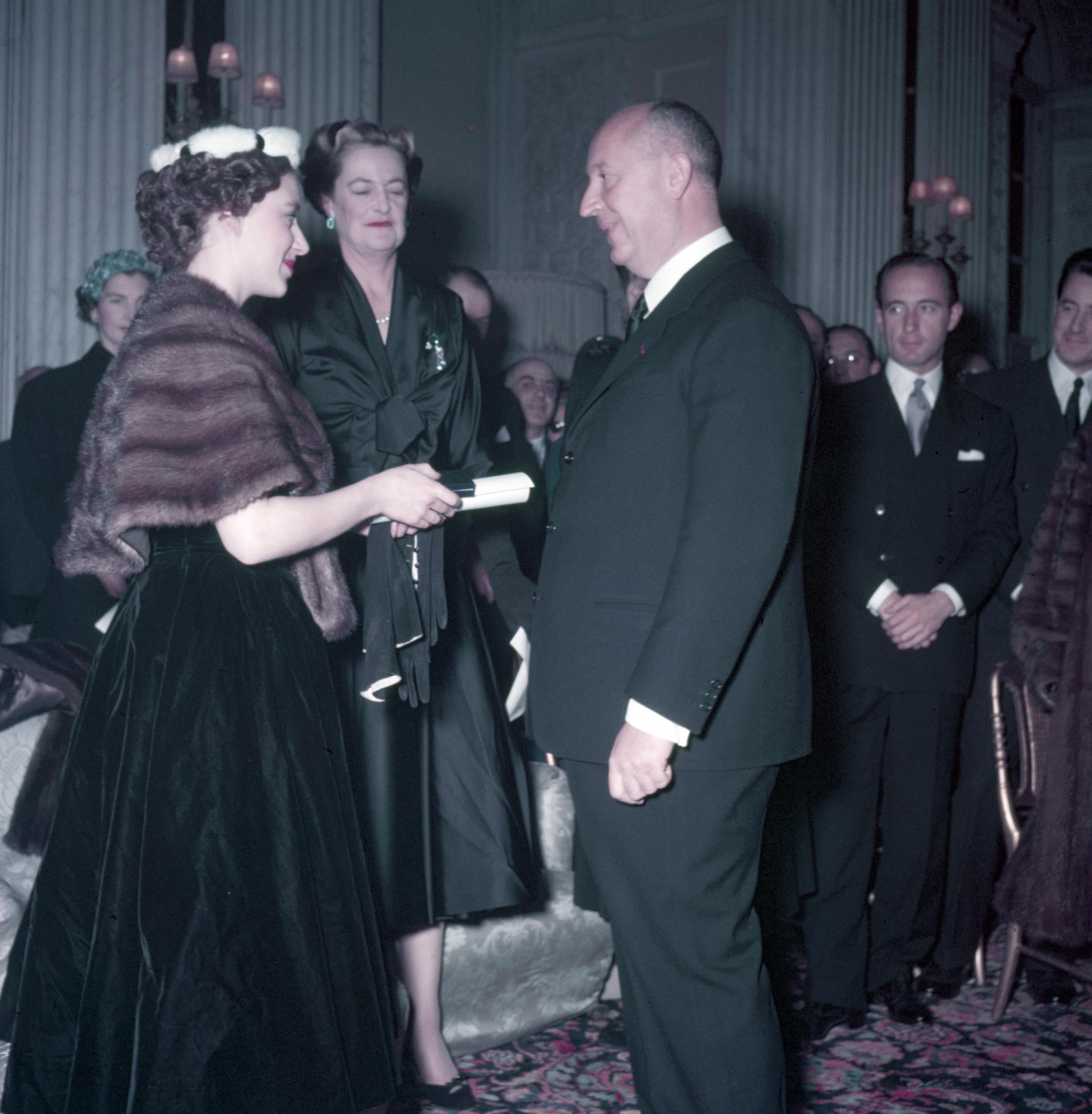 Princess Margaret (left), with the Duchess of Marlborough behind, presents Christian Dior with a scroll entitling him to Honorary Life Membership of the British Red Cross after the presentation of his Winter Collection at Blenheim Palace on 3 November 1954.