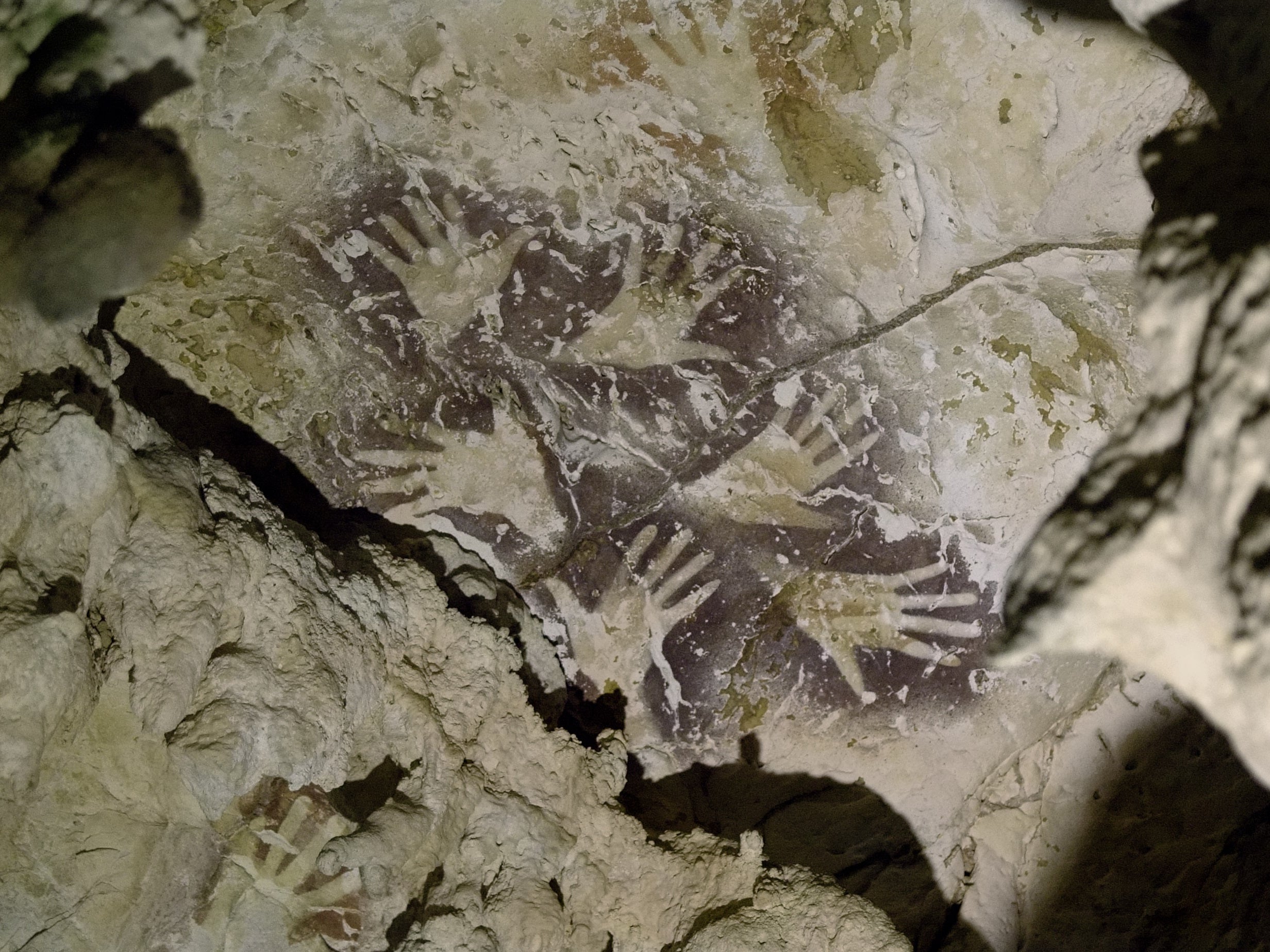 Composition of purple-coloured hand stencils superimposed over older reddish/orange hand stencils. The two styles are separated in time by at least 20,000 years.