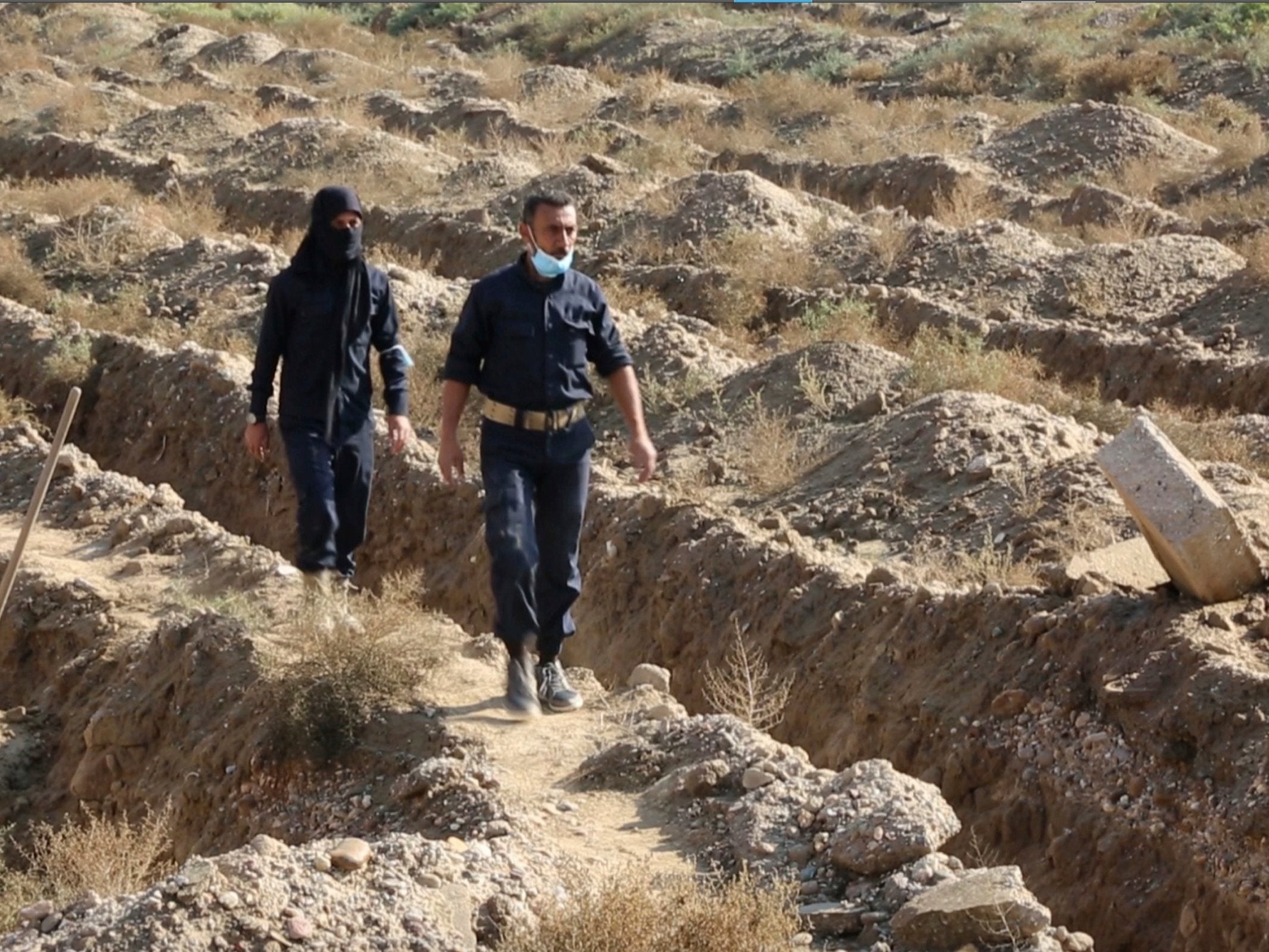 Syrian workers walk at the site of a mass grave believed to contain the bodies of civilians and Isis militants, in Raqqa