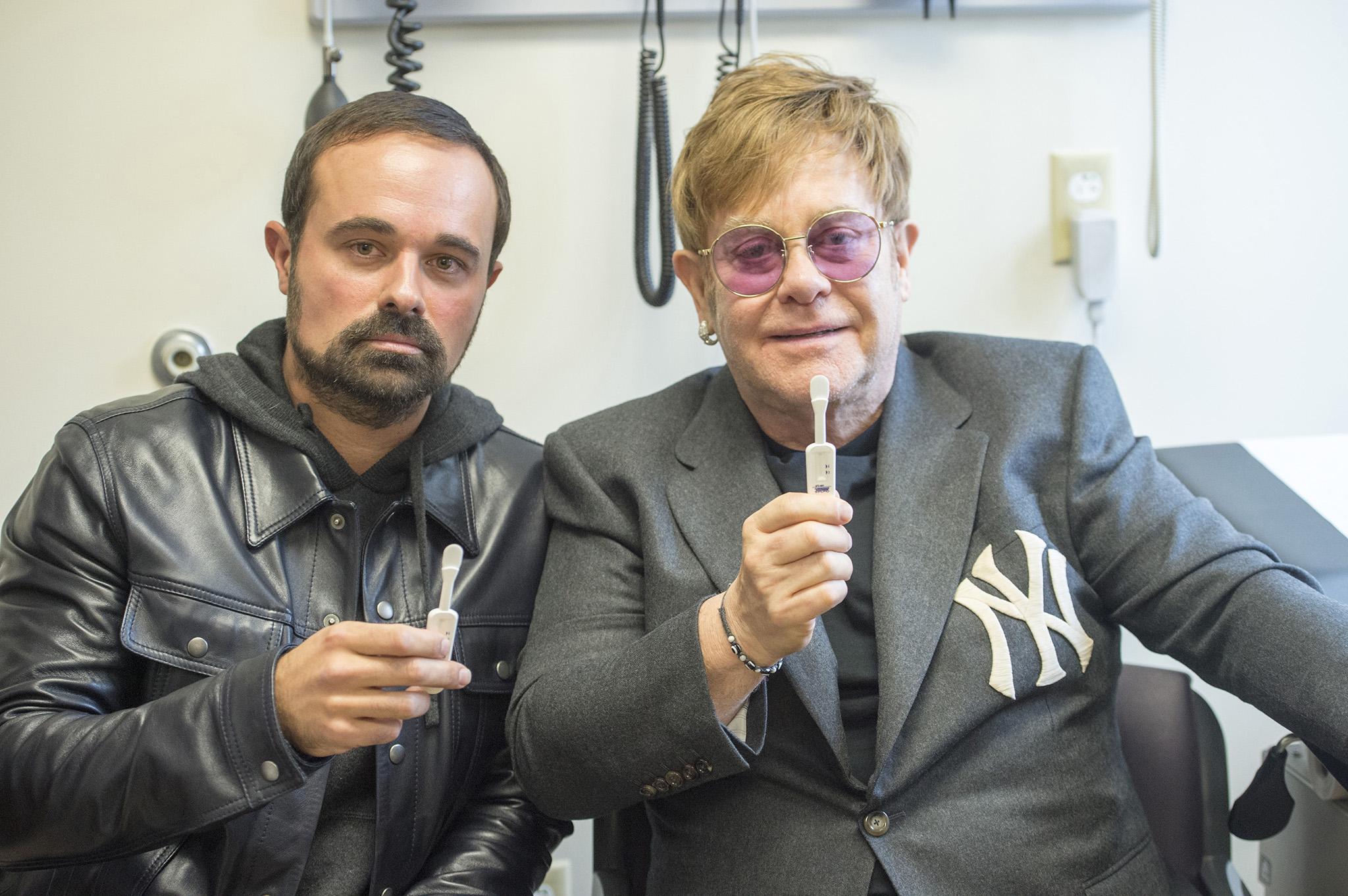 Sir Elton John and Evgeny Lebedev try out one of the most recent developments in testing, a simple swab, wiped around the mouth