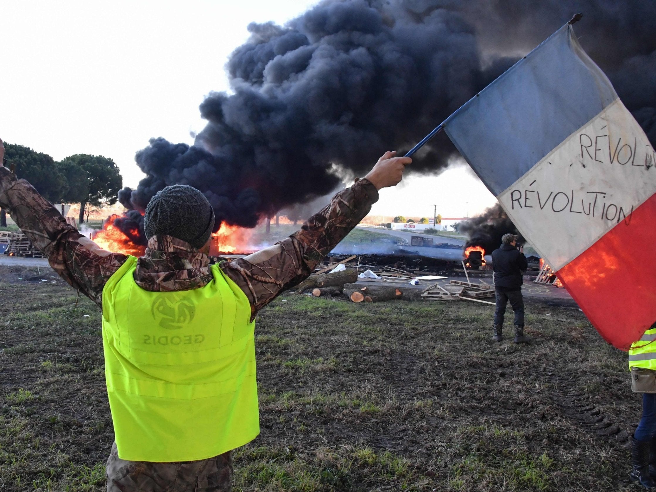 A man wearing a yellow vest waves a French flag in front of burning tyres at a road blockade during a protest against the rise in the price of oil and the cost of living