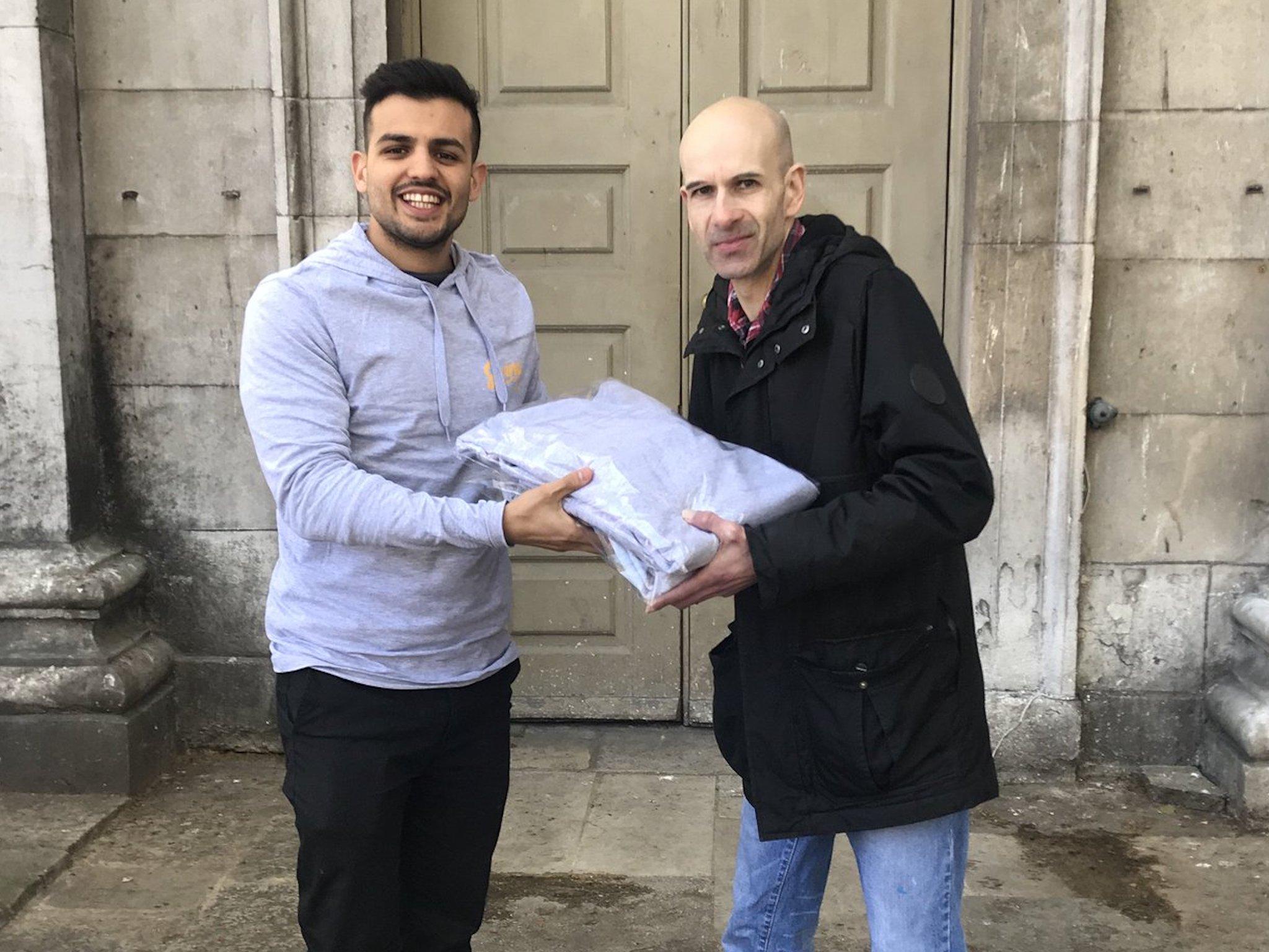 Varun Bhanot, left, the founder of Unhoused.org, gives a donation to a volunteer at the Spitalfields Crypt Trust