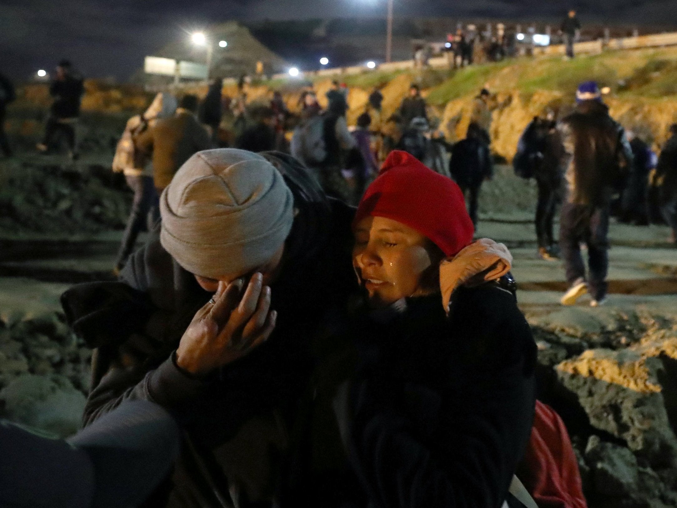 Migrants, part of a caravan of thousands from Central America trying to reach the US, wipe their eyes after tear gas was used