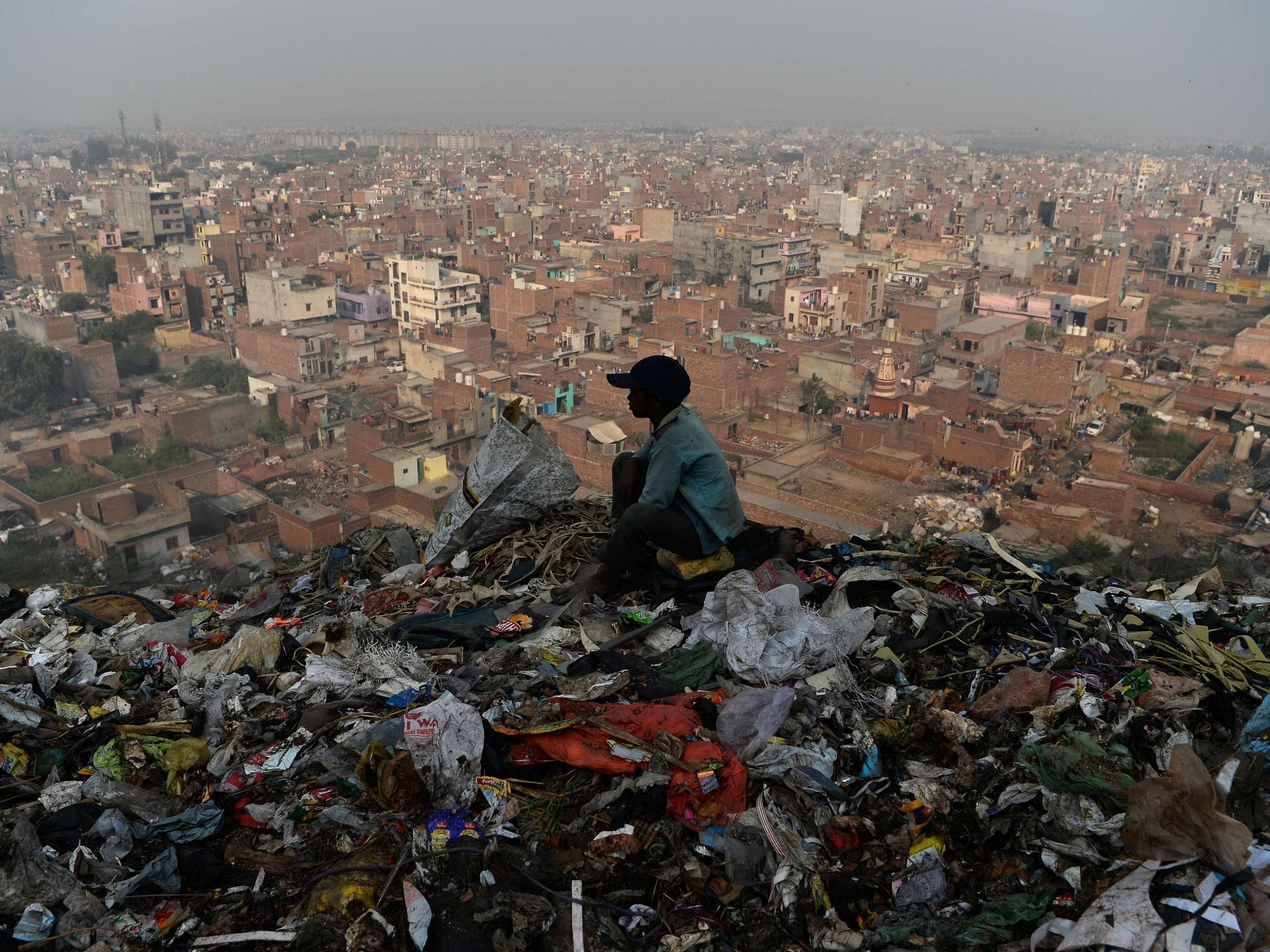 A young Indian ragpicker looks over the city after collecting usable material from a garbage dump at the Bhalswa landfill site in New Delhi