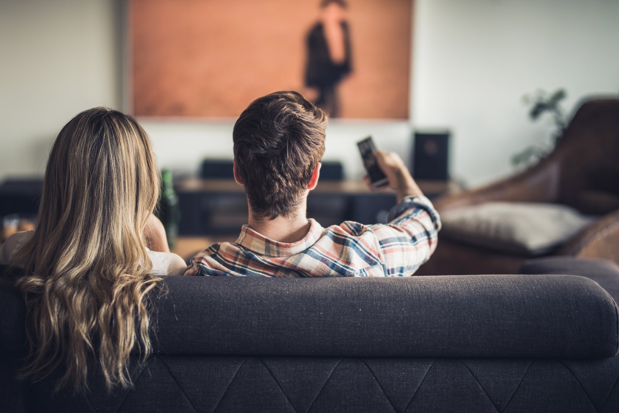 Back view of a couple watching TV on sofa at home.