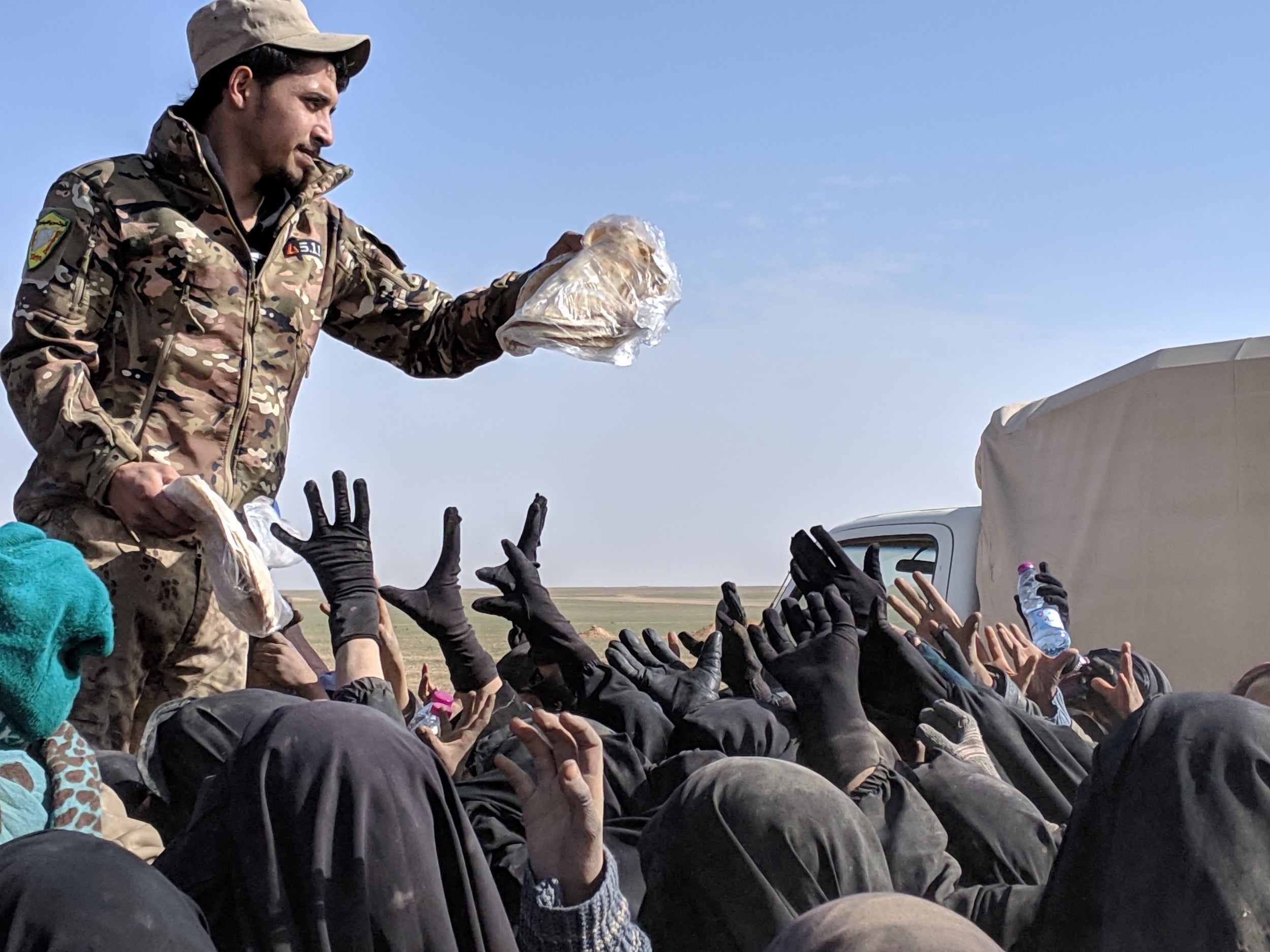 An SDF fighter hands out bread to women and children after they arrive from Isis-held areas in Deir ez-Zor today