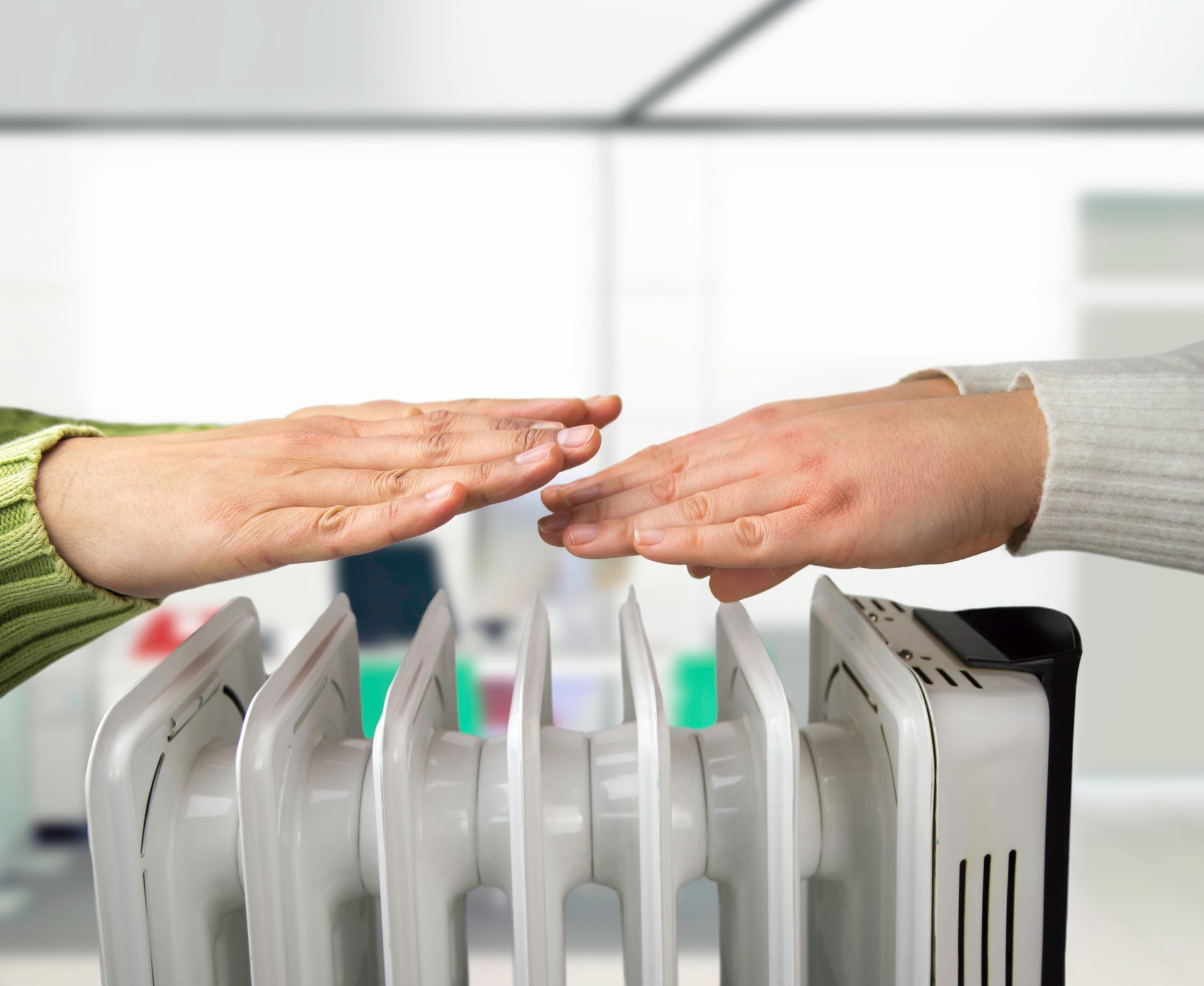 Coworkers warming up hands over electric heater at office in winter