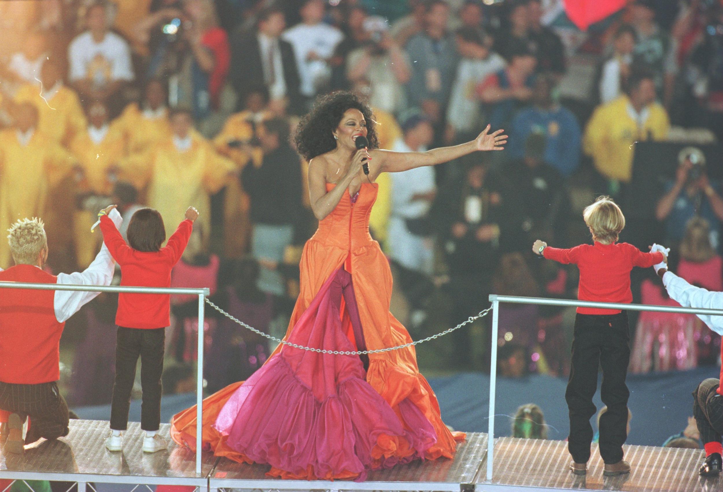 1996 - Diana Ross
<br><br>
For her halftime performance, singer Diana Ross wore a number of standout ensembles including this extravagant orange and pink gown. Earlier on in the show, she also sported a pink catsuit with a billowing gold cape