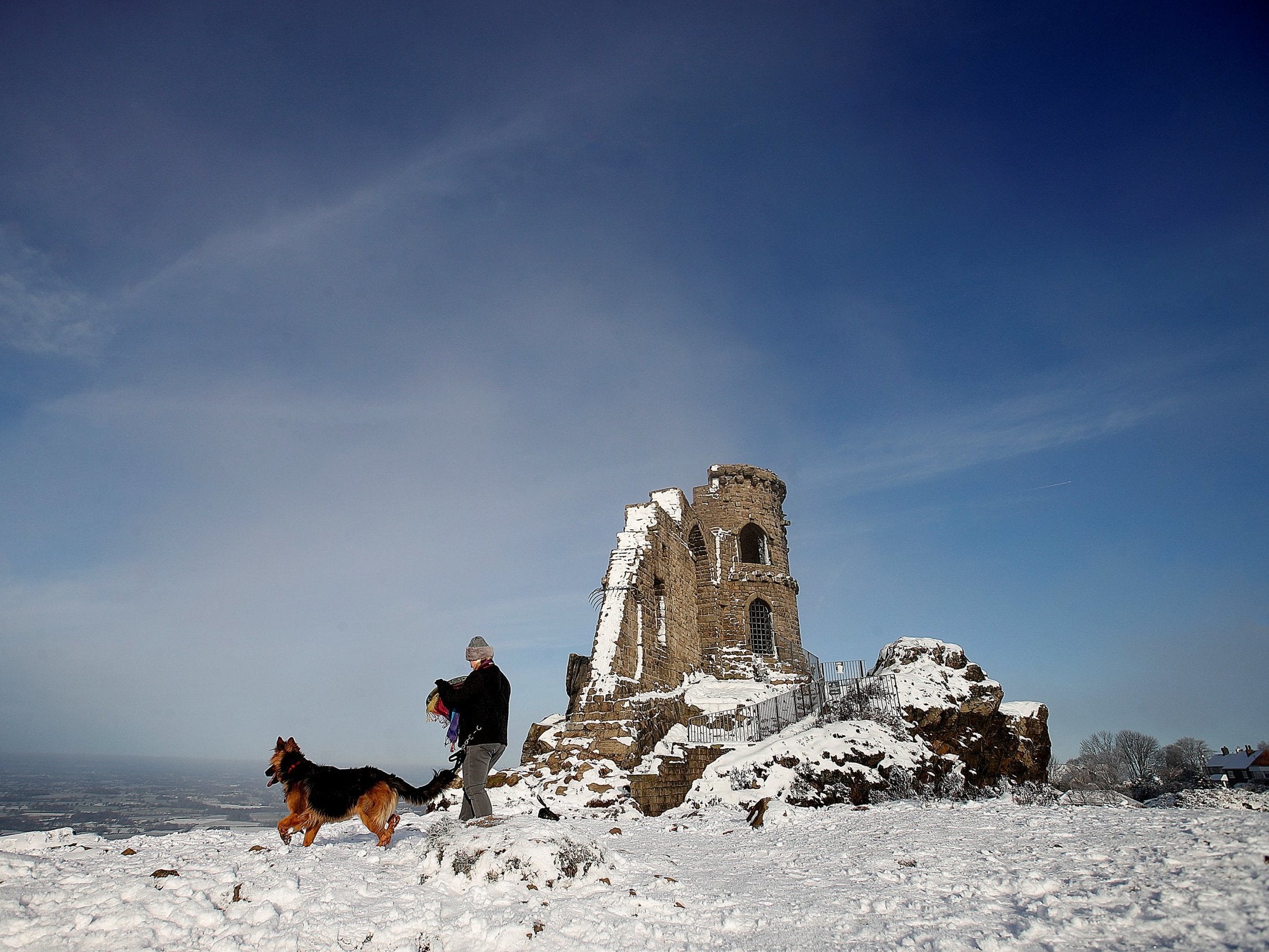 A dog walker walks through the snow past Mow Cop Folly, on the border of Cheshire and Staffordshire today (Reuters)