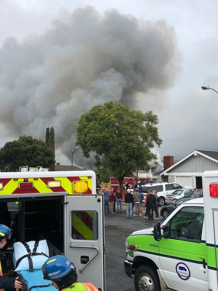 Ambulances stand at the ready as smoke rises from the house set ablaze by the crashed Cessna 414A