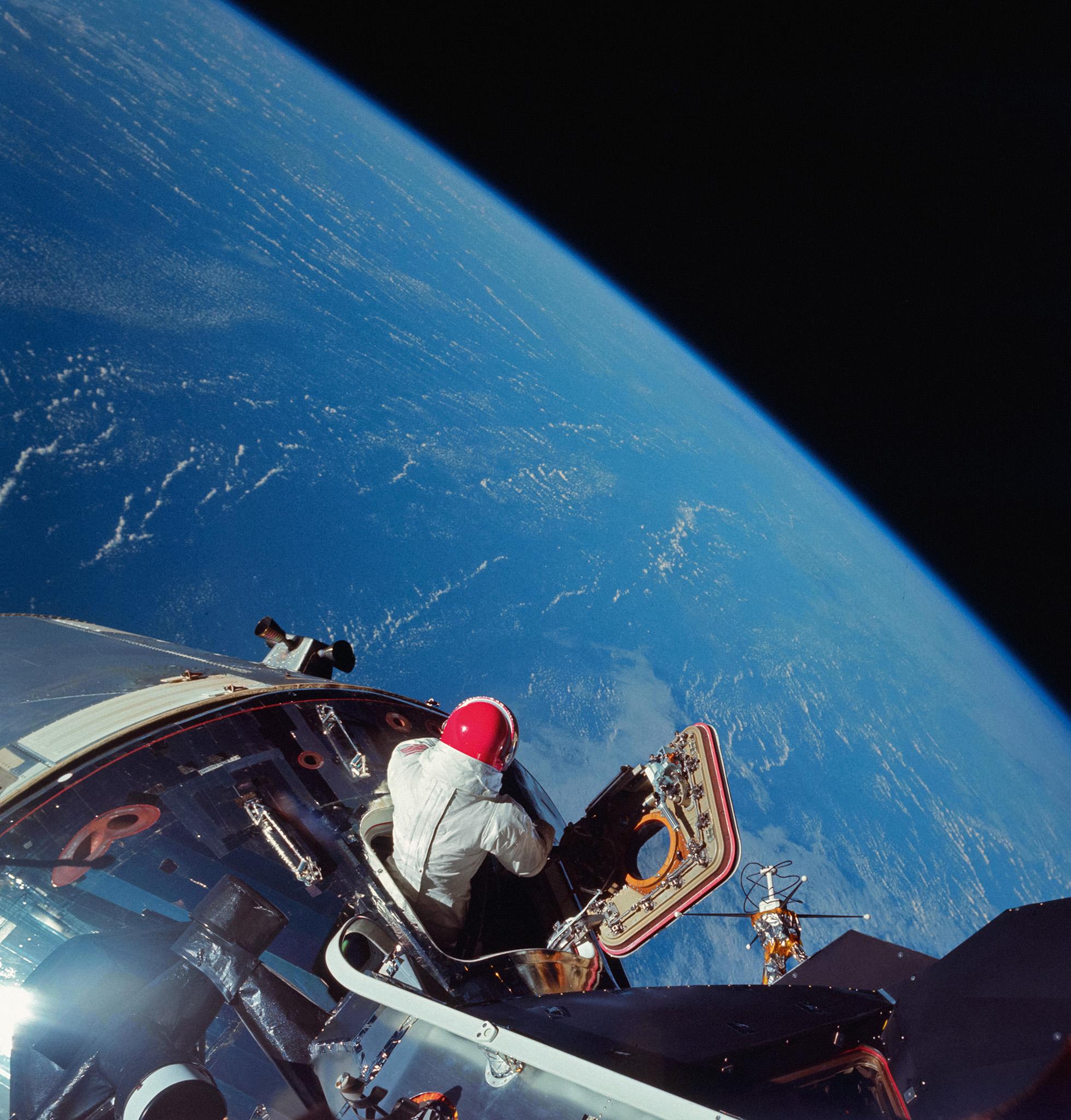 Apollo 9 CM pilot Dave Scott emerges from the hatch, testing some of the spacesuit systems that will be used for lunar operations. The photo was taken from the hatch of the docked LM by Rusty Schweickart in March 1969.