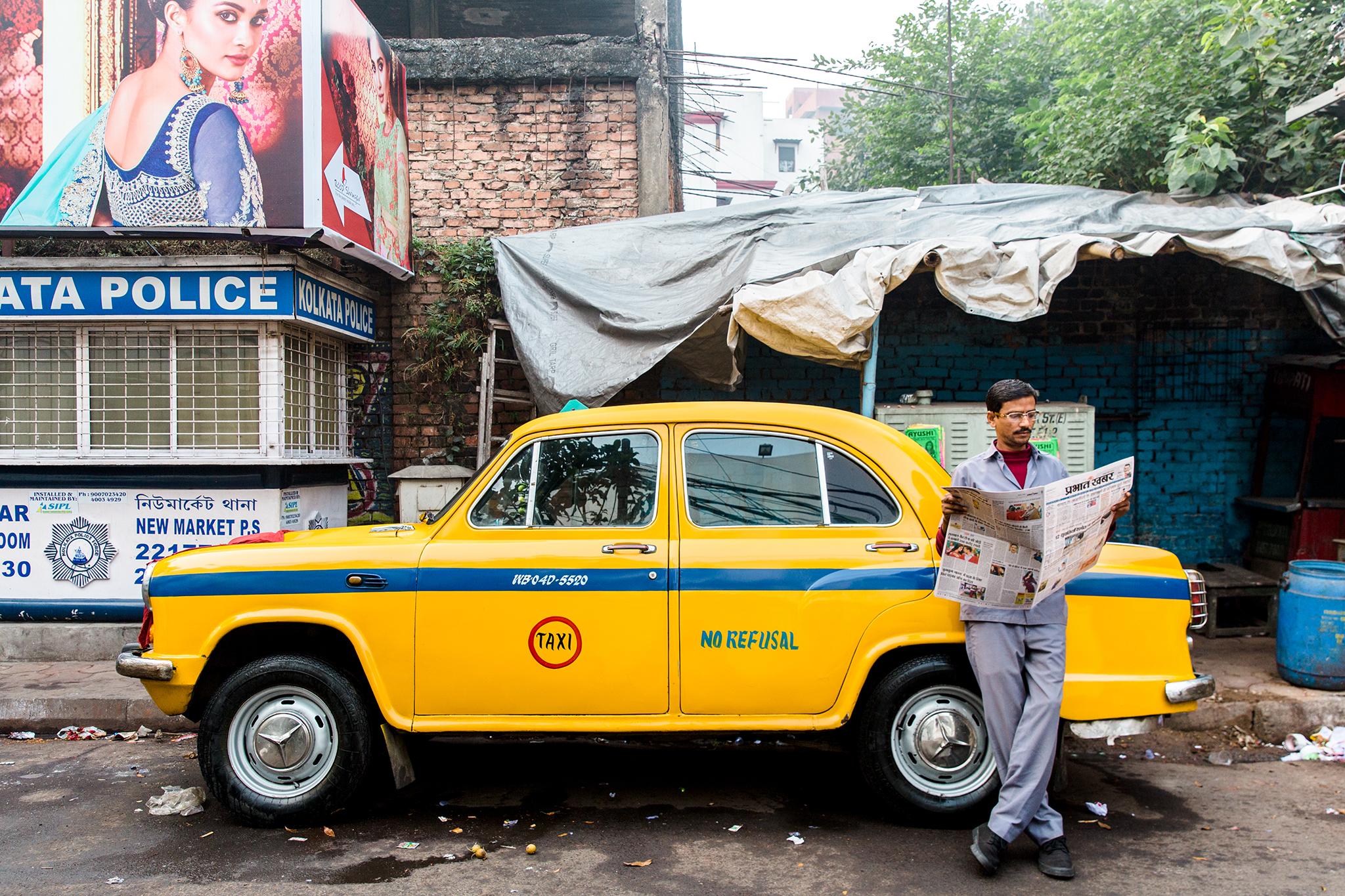"A taxi driver leans against his yellow Ambassador cab — one of the icons of the city — reading a newspaper before the day begins" - Annapurna Mellor