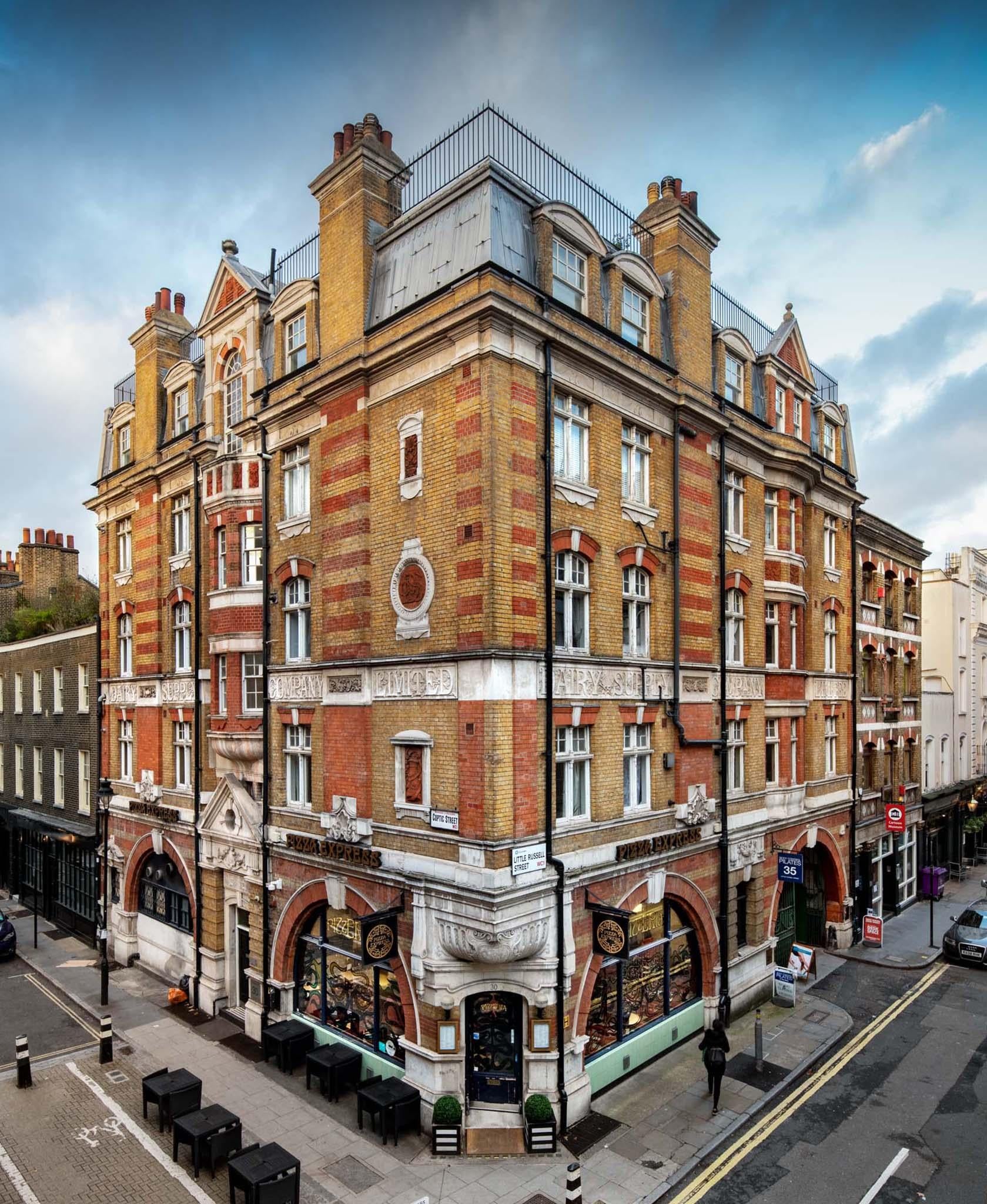 Originally constructed in 1888 for the Dairy Supply Company, 30 Coptic Street and 35 Little Russell Street were once the place of manufacture of the iconic milk churn. It is here that they made 17 gallon galvanised iron containers, designed for transporting milk by rail. The company was heavily associated with George Barnham, who invented the containers and went on to become chair of the British Dairy Farmers Association, Mayor of Hampstead and High Sheriff of Middlesex and was knighted in 1904.
The buildings still pay homage to their days as the headquarters of the first major manufacturer of dairy equipment, with its original signage, made of Portland stone, still intact. The exterior features ornate brick decoration which advertised the Dairy Supply Company Limited.
Listed Grade II