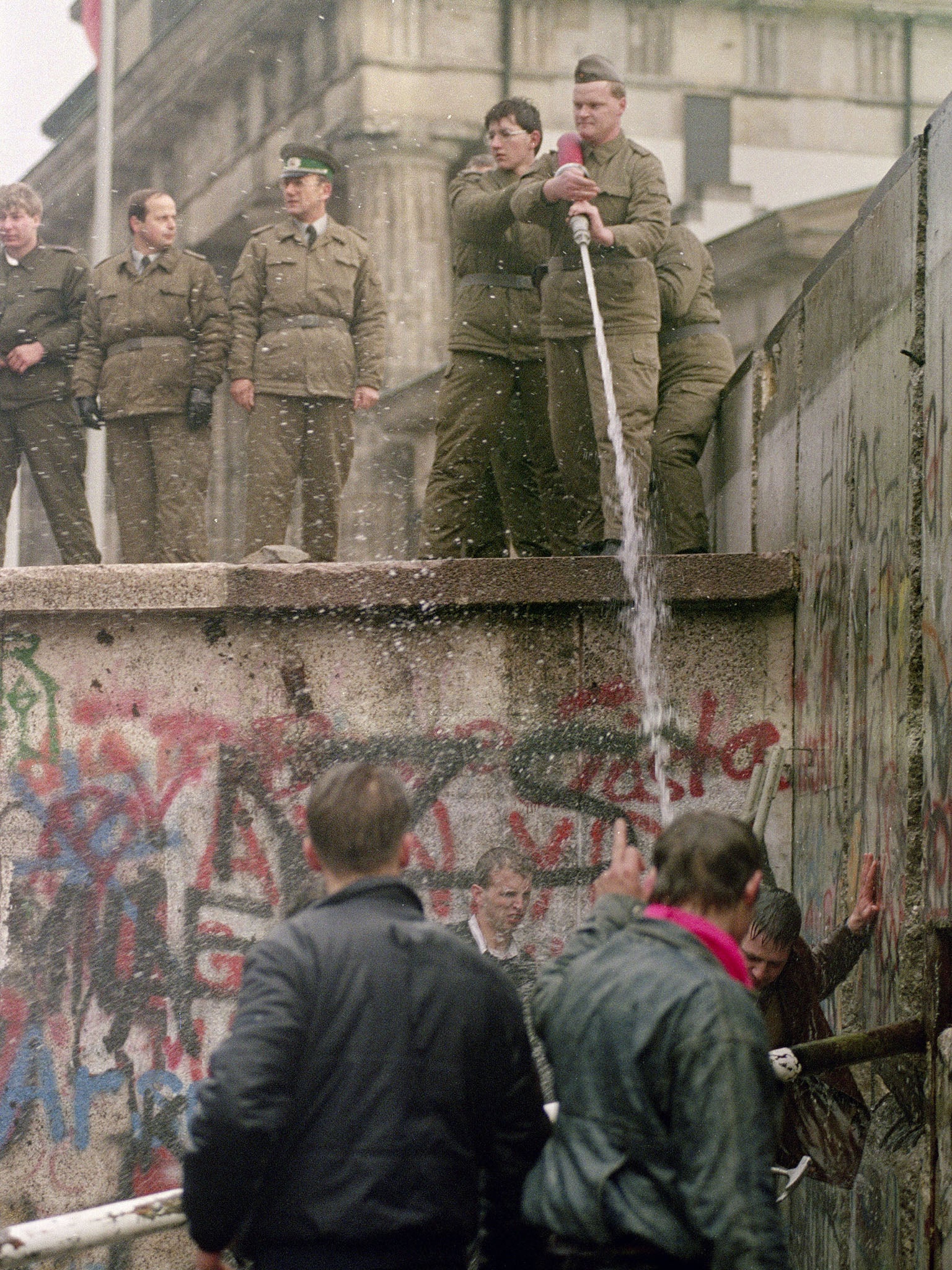 East German police atop the Berlin Wall spray Berliners with water on 11 November 1989 (AFP/Getty)