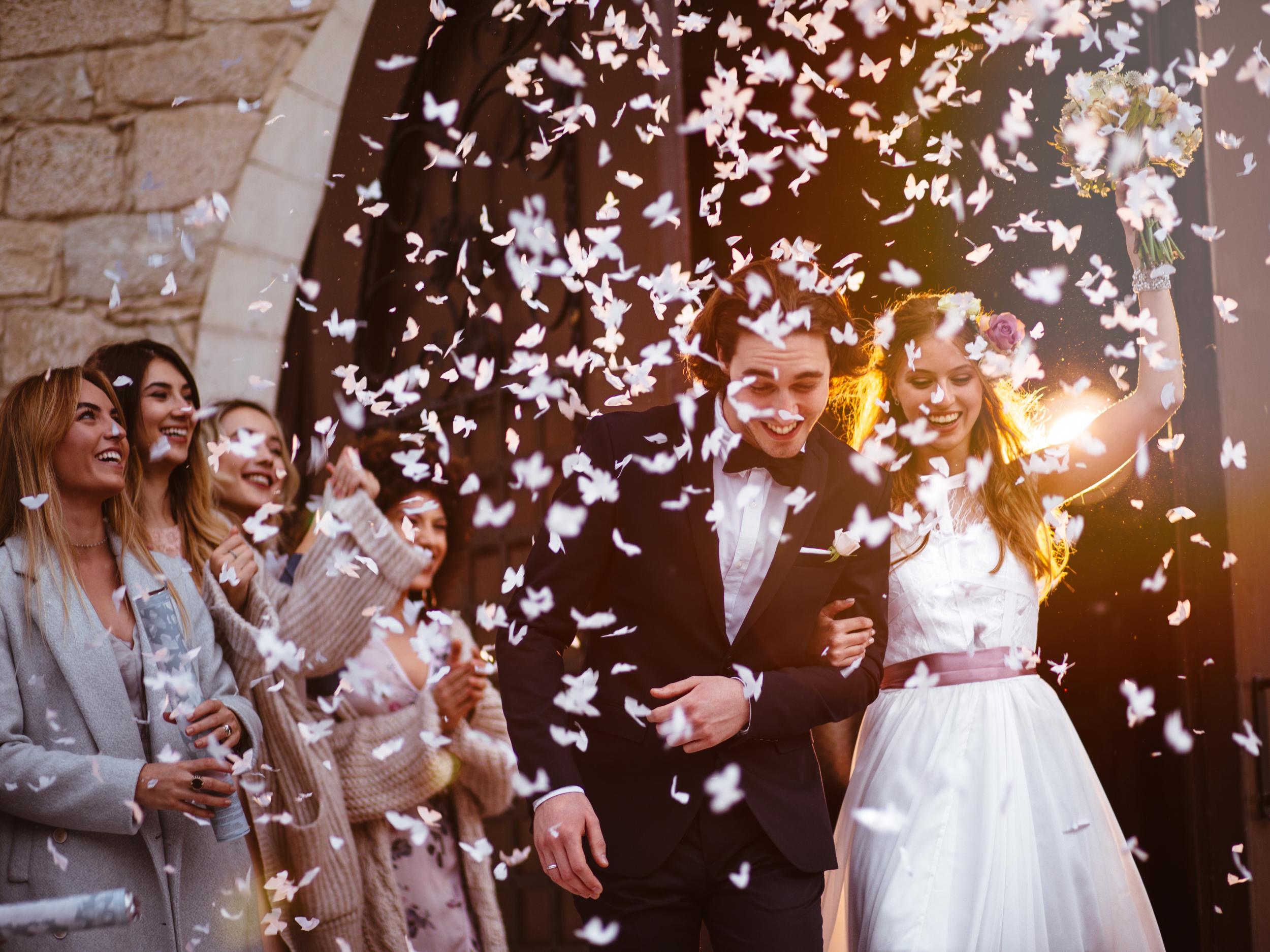 Newlywed husband and wife walking out of church and celebrating marriage with guests throwing confetti