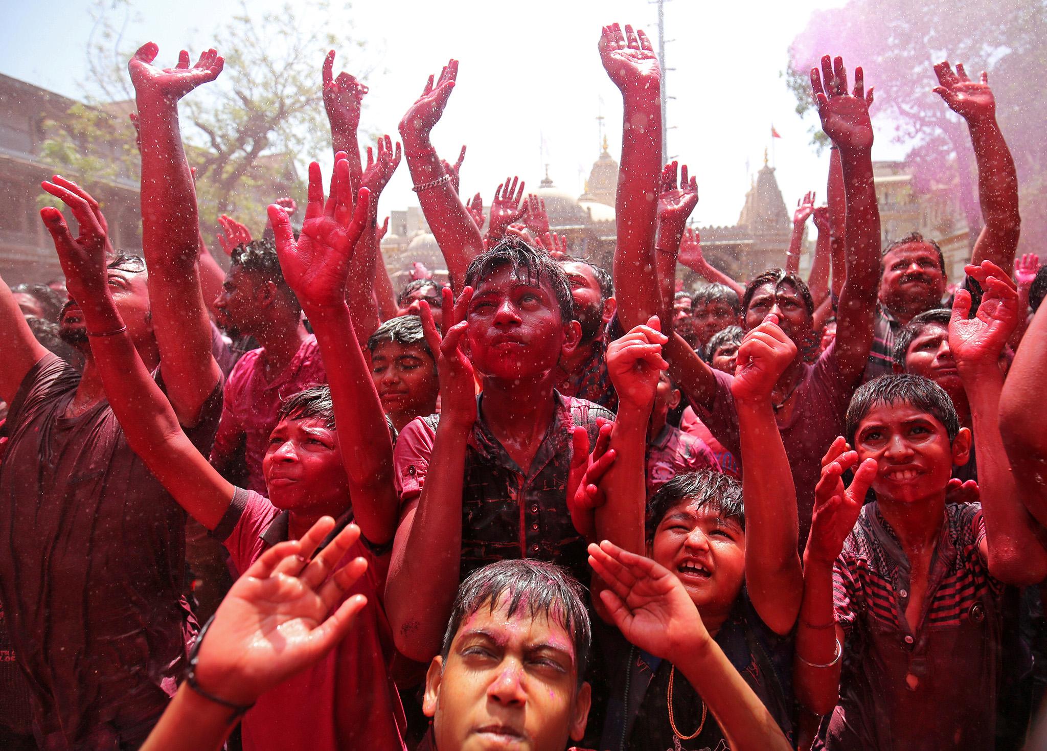 Hindu devotees raise their hands in prayer as they are sprayed with colour by a priest during Holi celebrations in Ahmedabad, India
