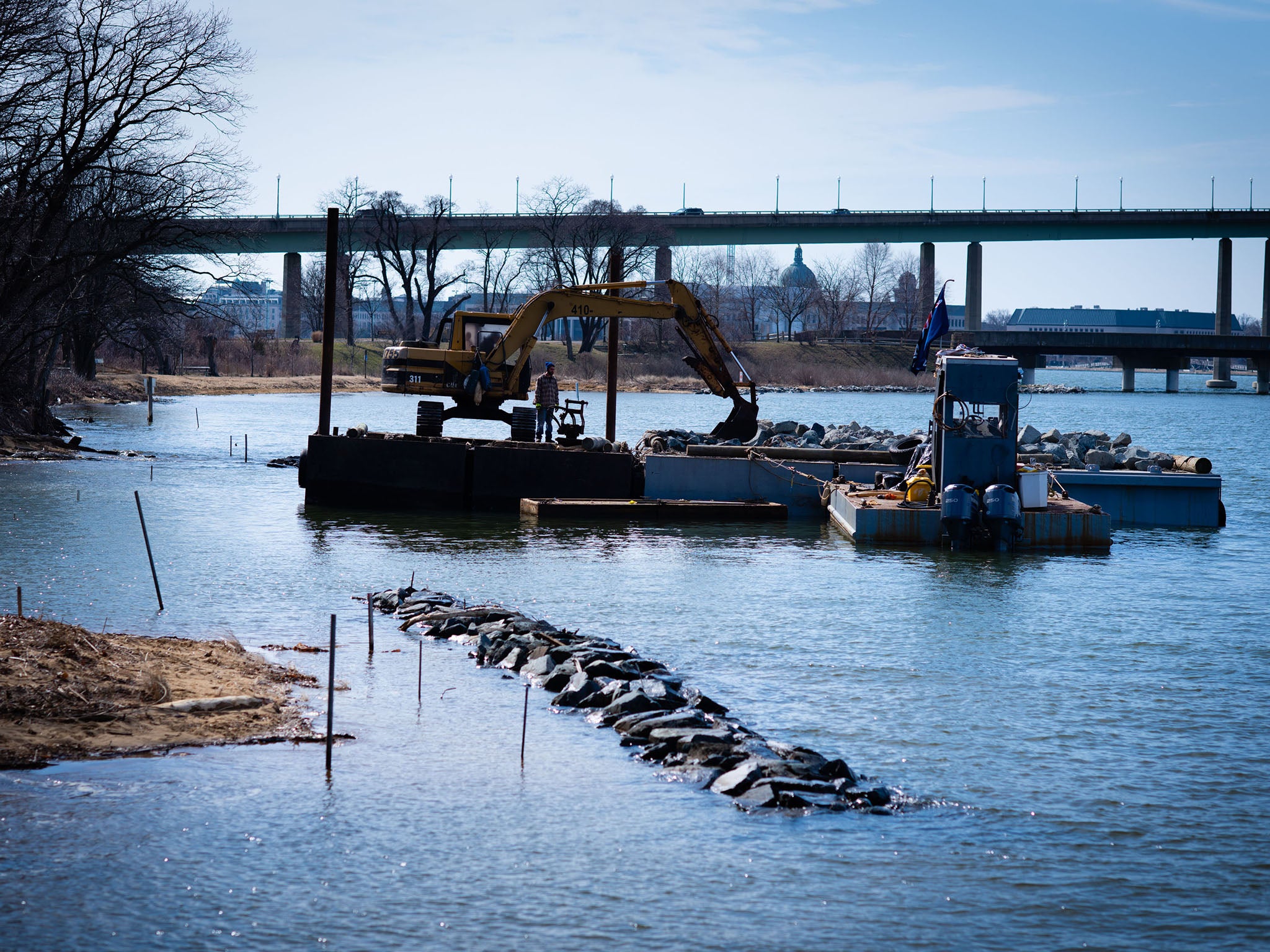 A contractor puts rocks in the water to make a barricade in front of a home on the river to construct a living shoreline in front of an eroded cliff to protect it and the home from damage