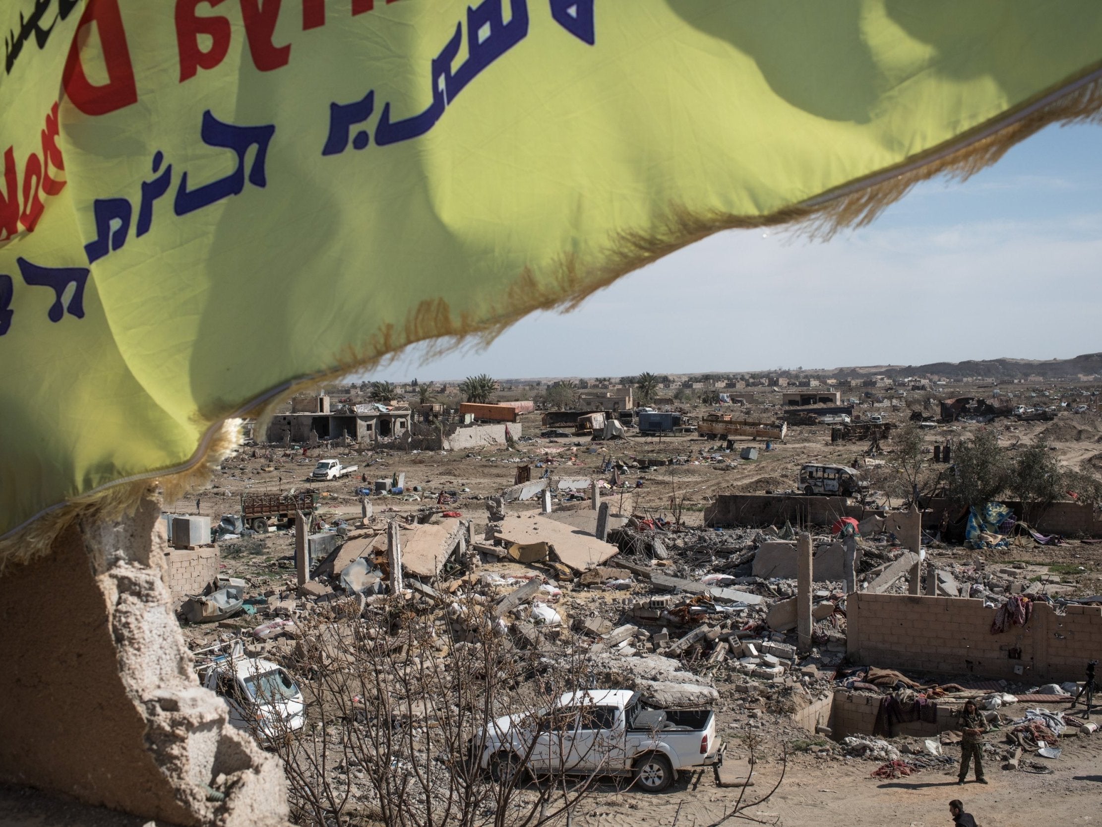 A Syrian Defence Forces flag flies over a destroyed Isis camp in Baghouz