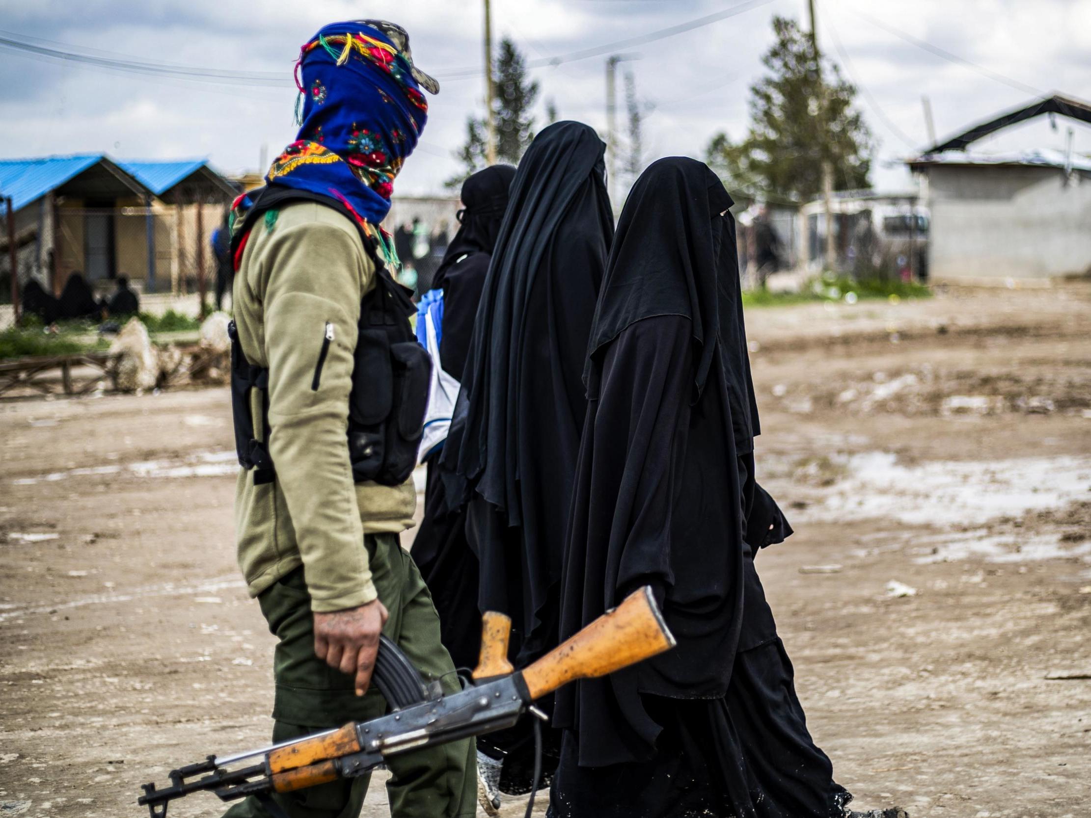 Foreign women living in al-Hol camp, which houses relatives of Isis members, walk under the supervision of a fighter of the Syrian Democratic Forces on 28 March 2019