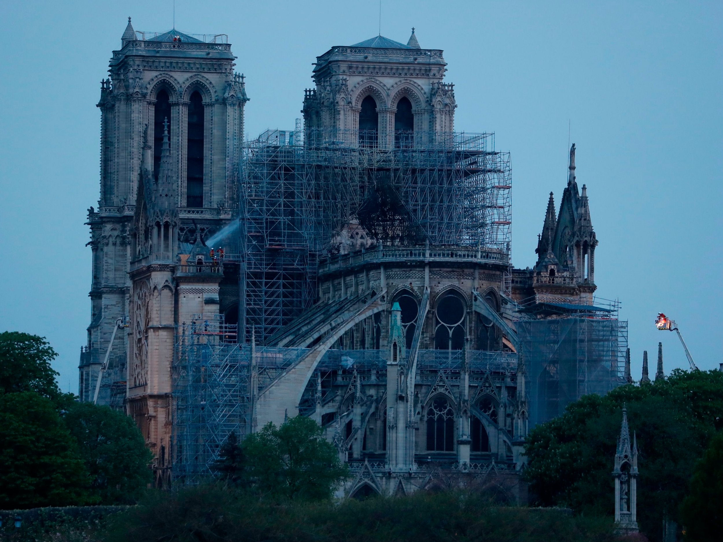 Firefighters (L and R) continue work to extinguish the fire at Notre Dame in Paris as dawn breaks on 16 April