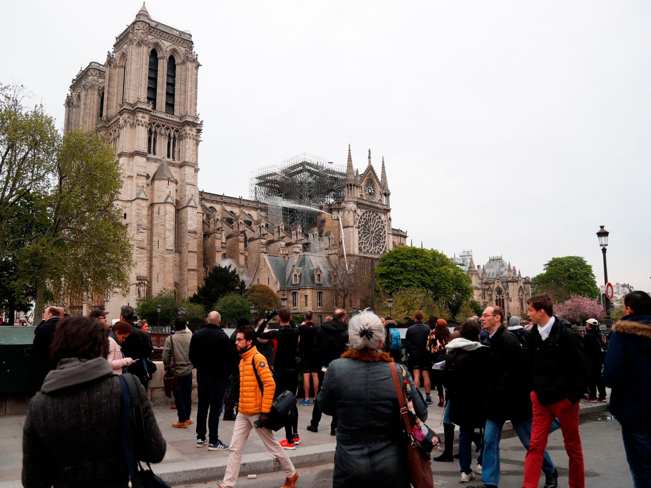 Onlookers stand on the banks of the Seine river in Paris on 16 April 2019 and view the aftermath of a fire at Notre Dame cathedral that caused its spire to crash to the ground. (AFP/Getty Images)