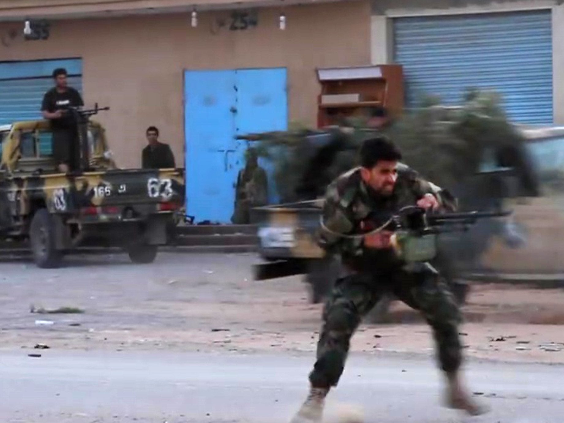 A fighter, thought to be in a southern suburb of Tripoli, runs while firing a machine gun