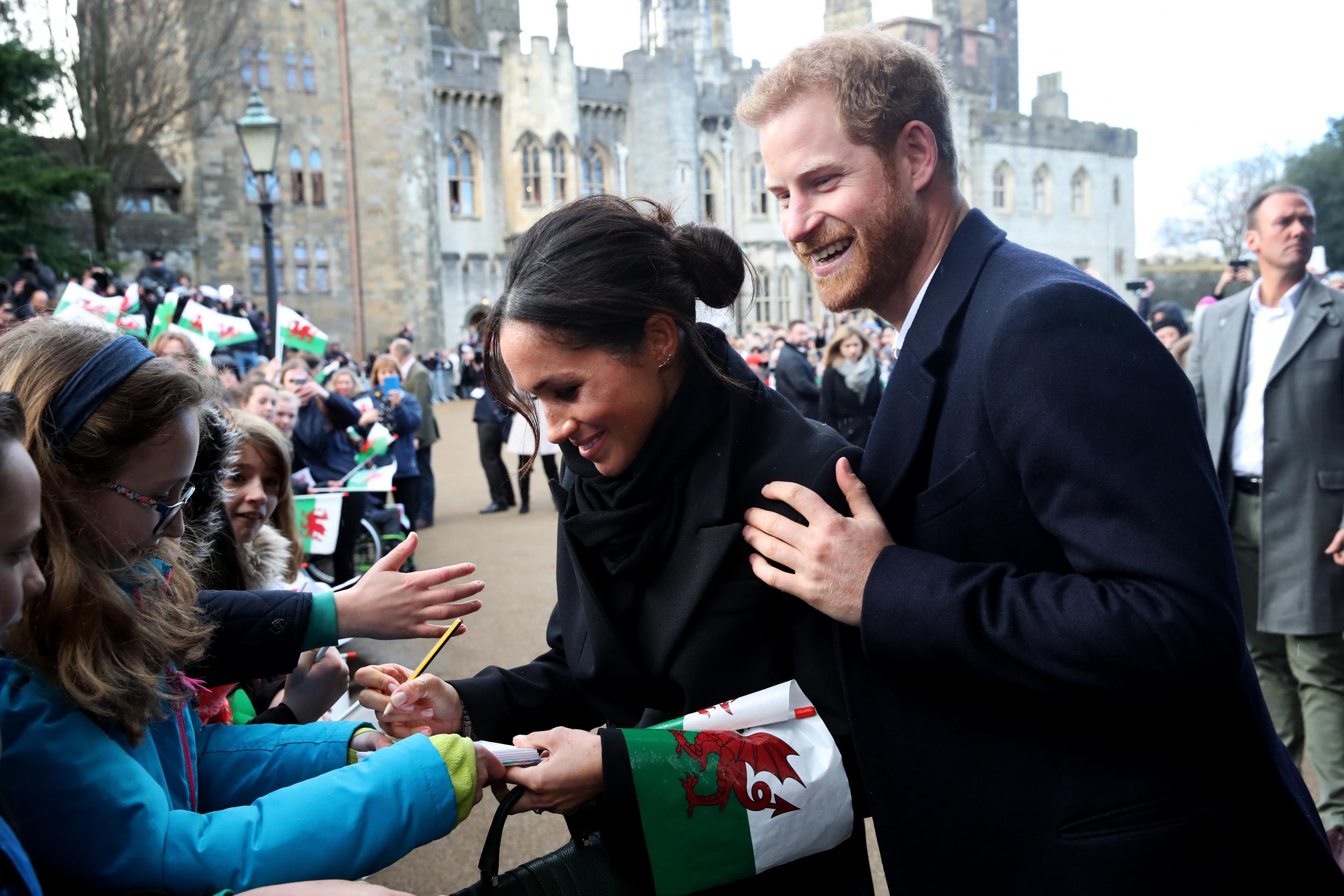 Prince Harry and Meghan Markle sign autographs and shake hands with children as they arrive to a walkabout at Cardiff Castle on January 18, 2018 in Cardiff, Wales