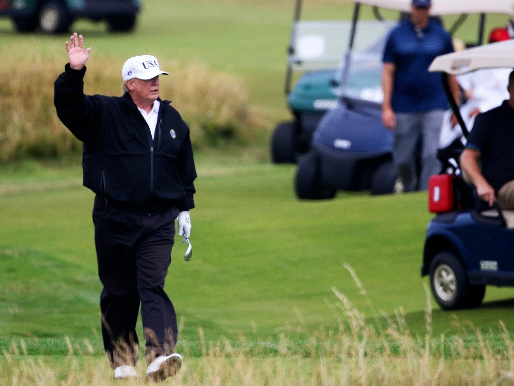 President Donald Trump waves to protesters while playing golf at Turnberry golf club in the middle of his official trip to Europe