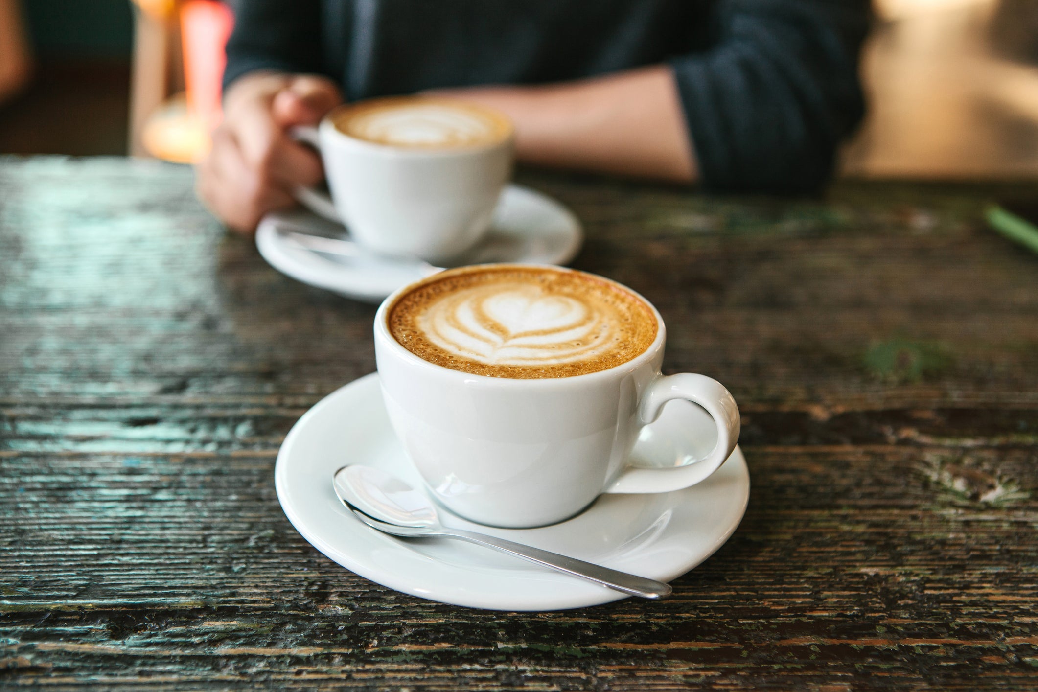 Two cups of coffee on a wooden table, the girl holds in her hand one cup of coffee in the background