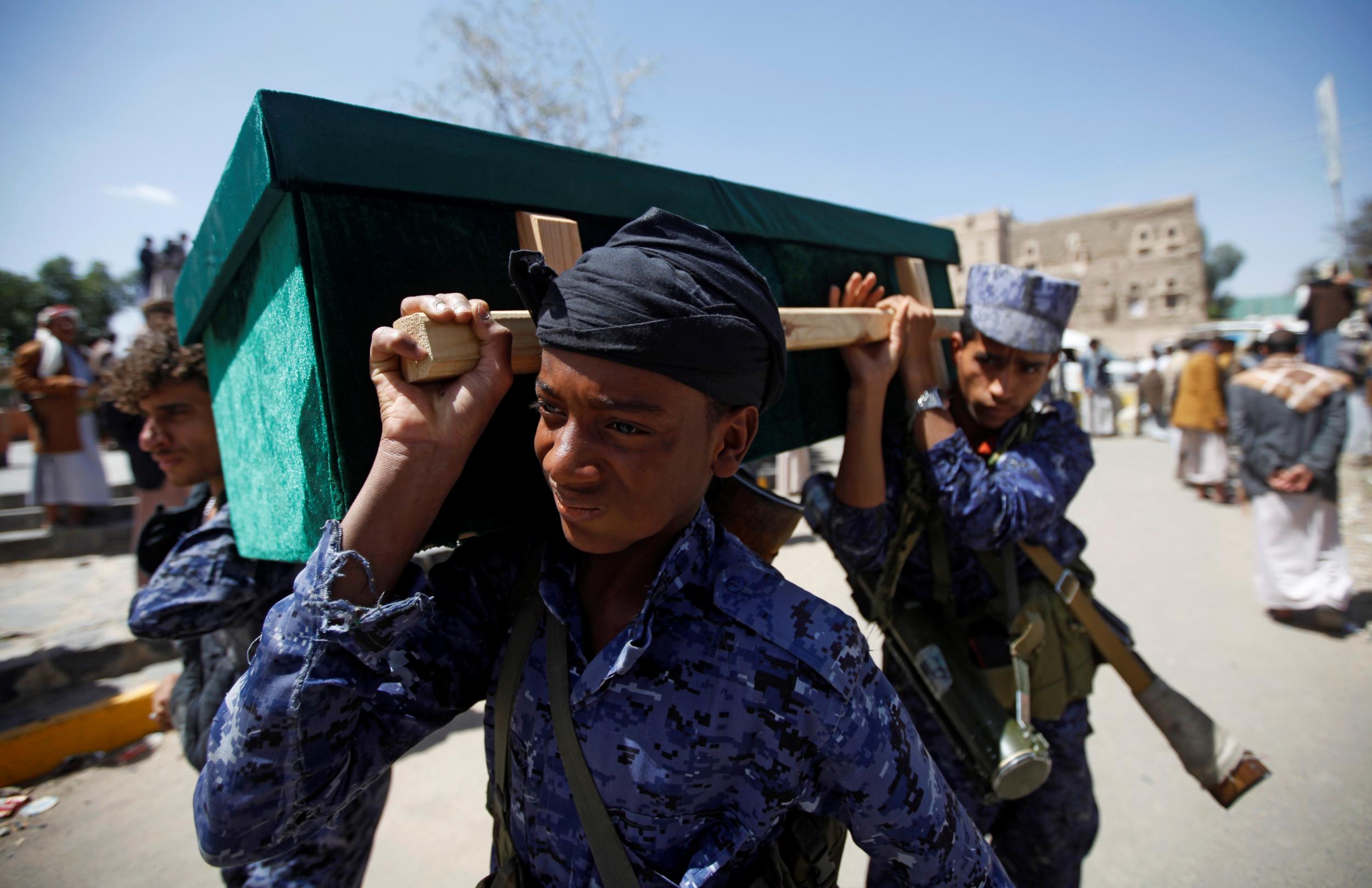 Houthi security officers carry a coffin during a funeral of people killed by a March air strike