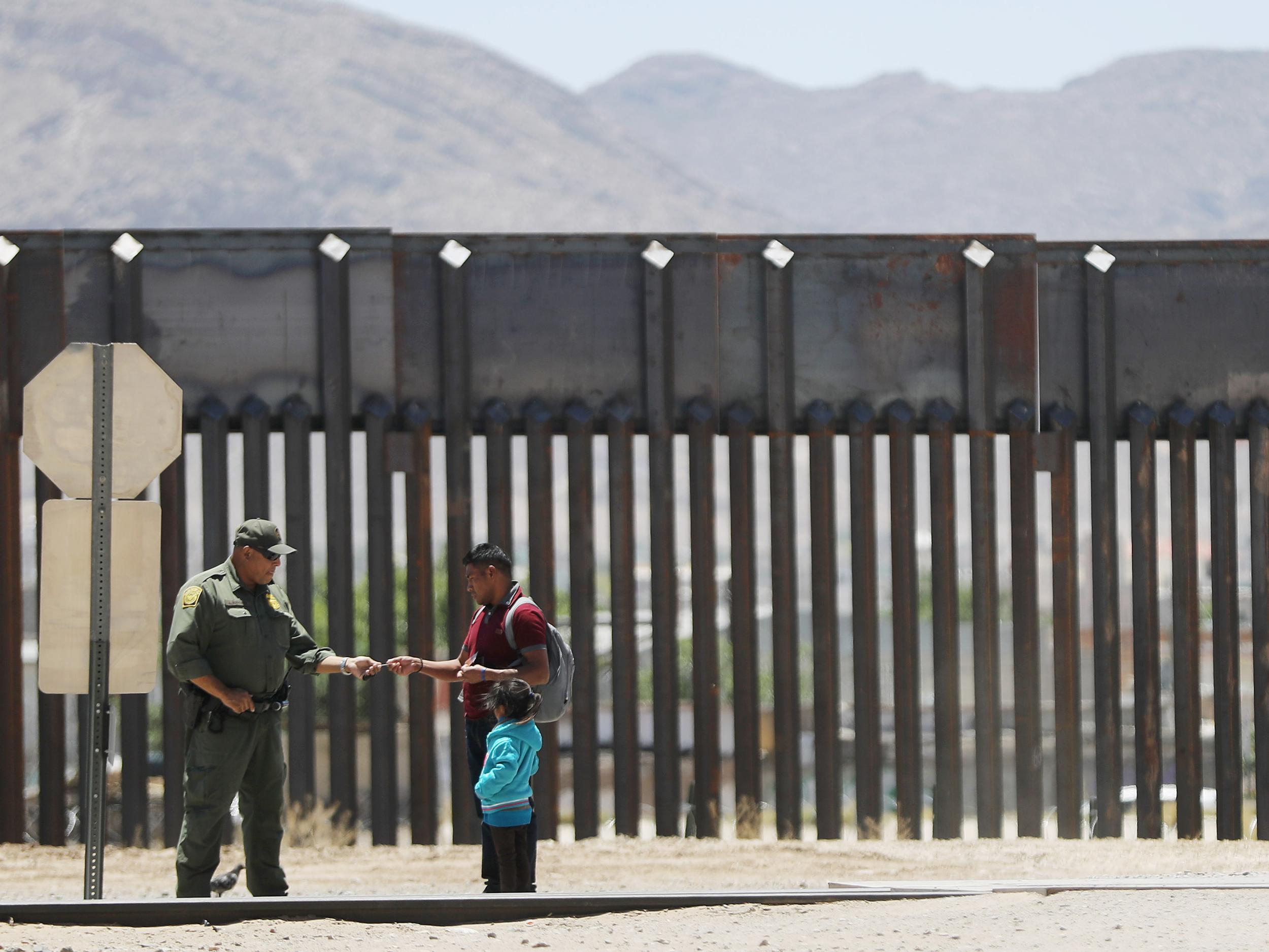 A US Border Patrol agent (L) checks the identification of a migrant with a child as they are detained after crossing to the US side