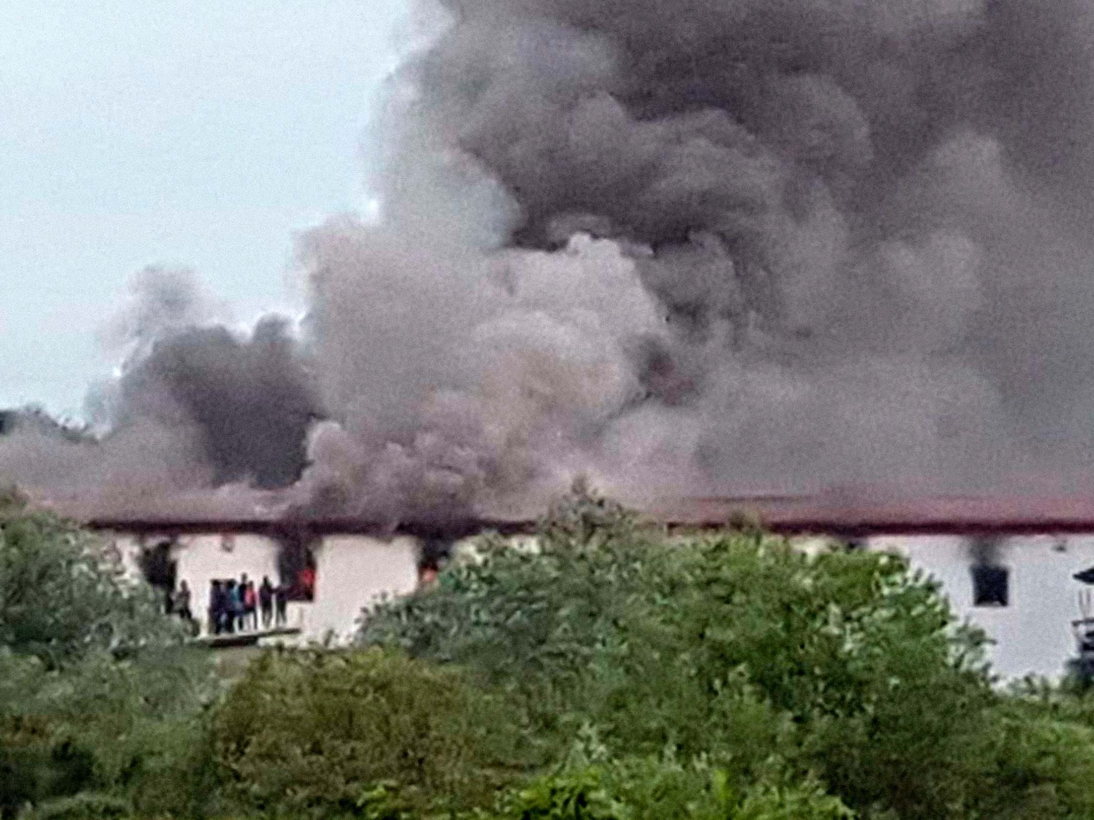 Migrants stand next to a burning dormitory at the camp near the border with Croatia